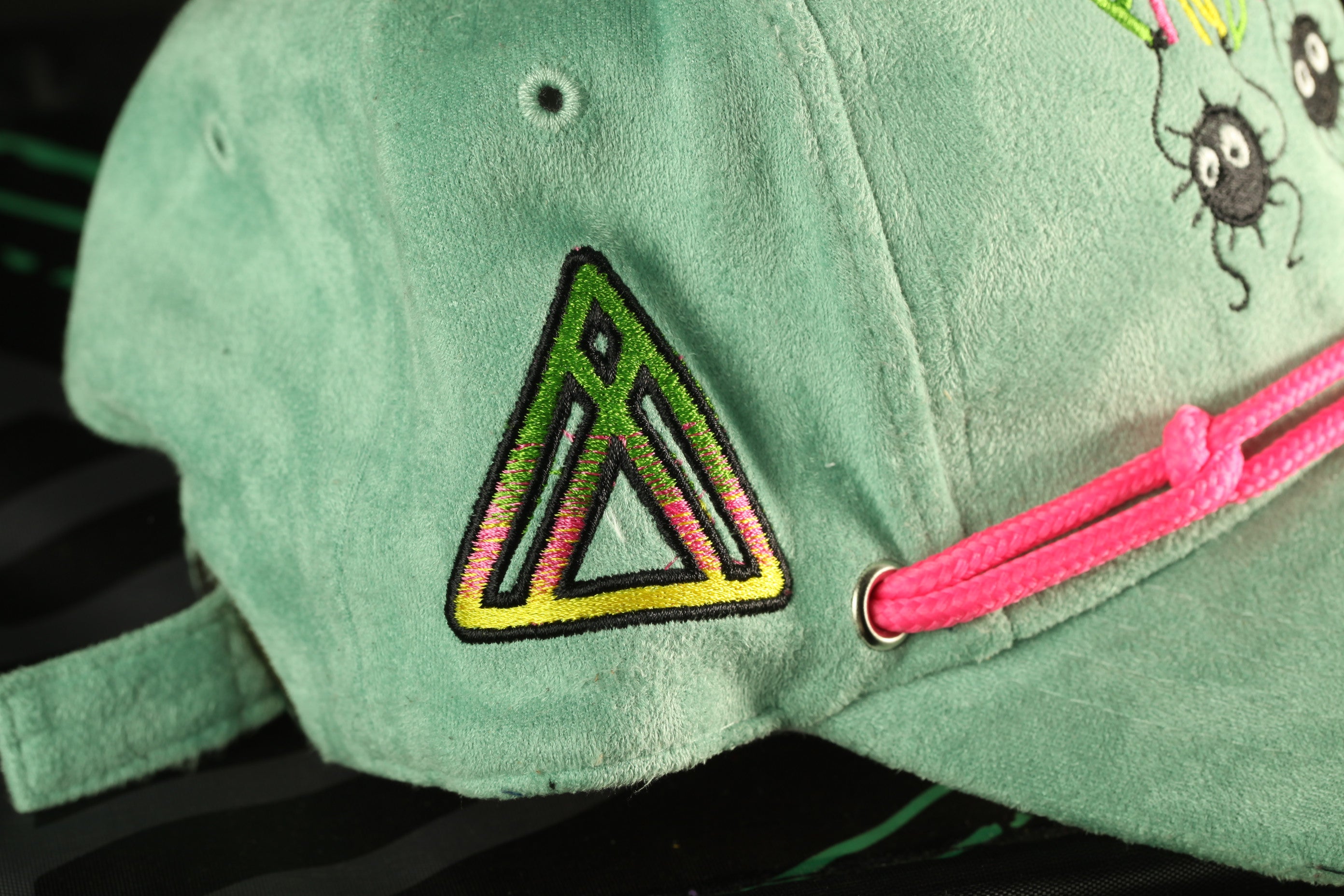 A close-up view of a green baseball cap with a colorful triangle embroidered on it.