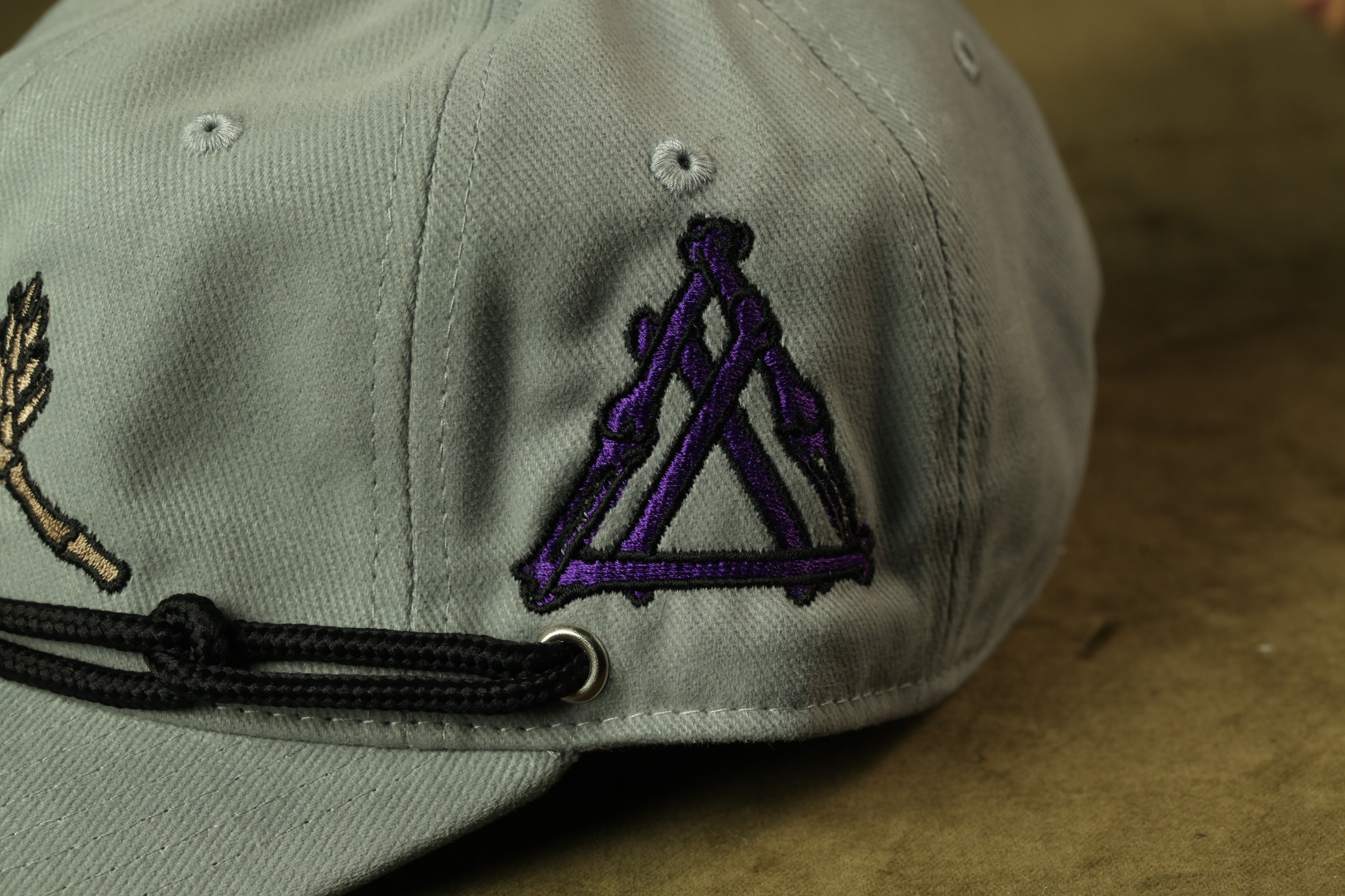 A close-up view of a gray baseball cap with a purple triangle embroidered on the front.
