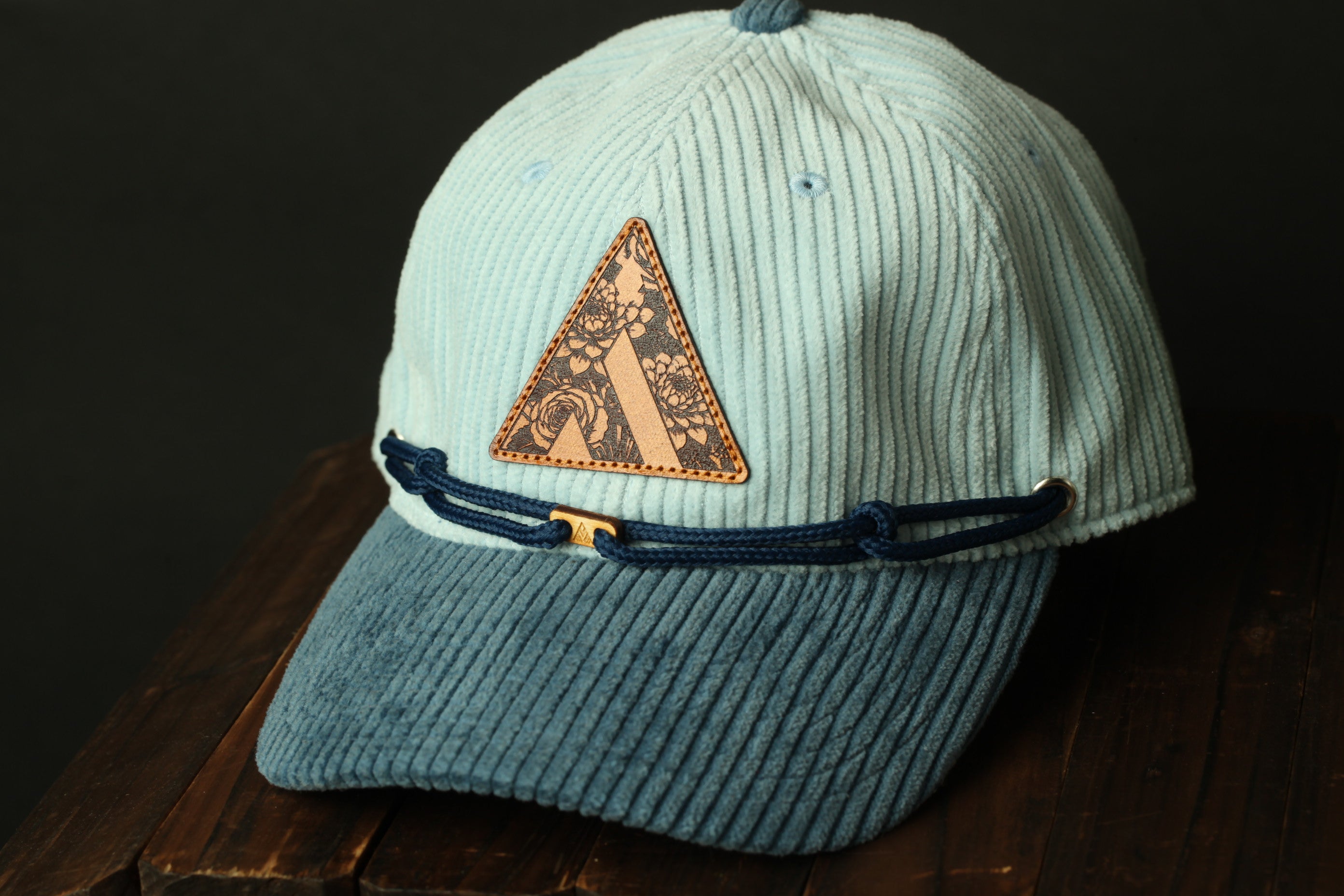 A light blue baseball cap with a patterned patch on the front, resting on a wooden surface.