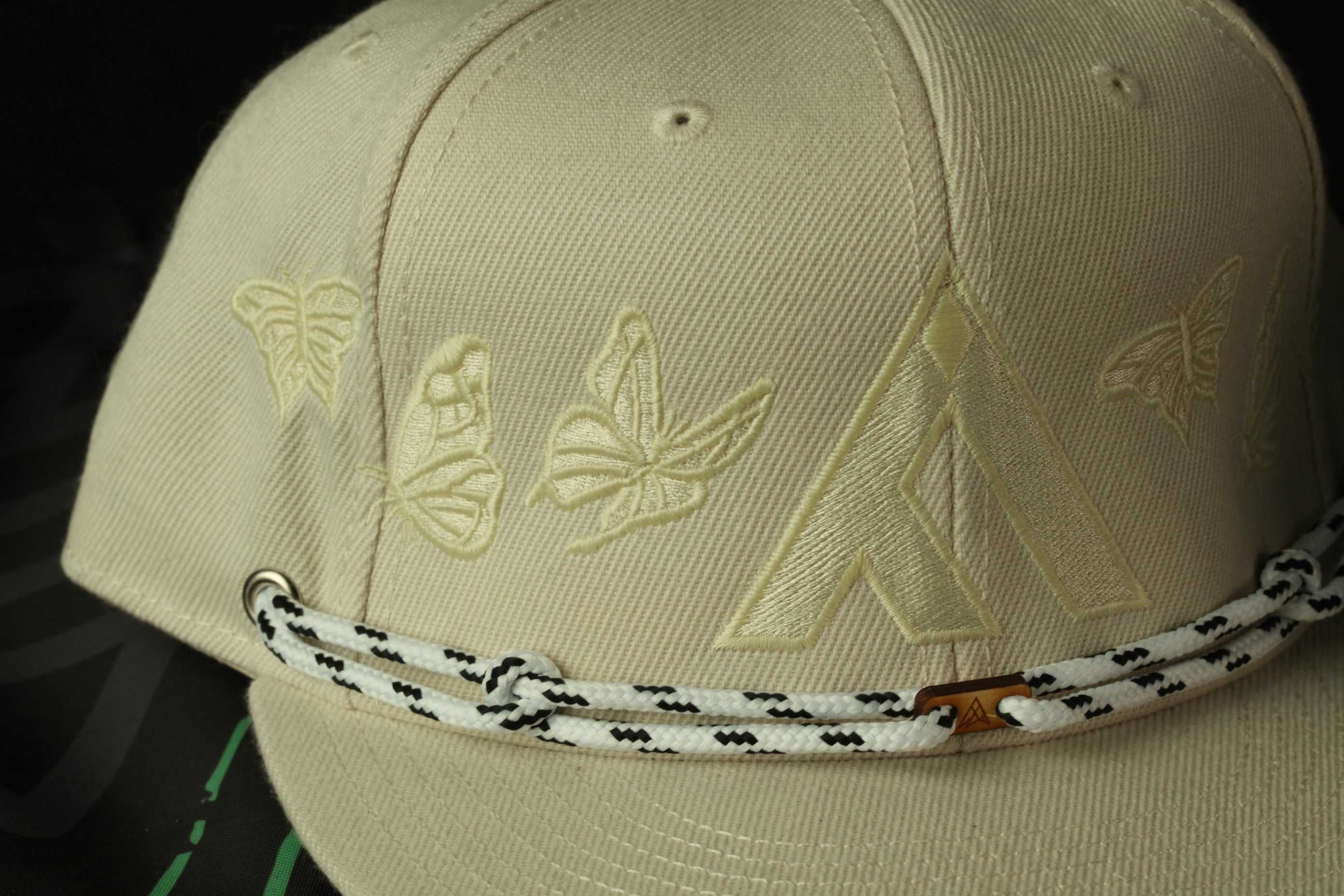 A close-up view of a beige baseball cap with a white and black braided strap.
