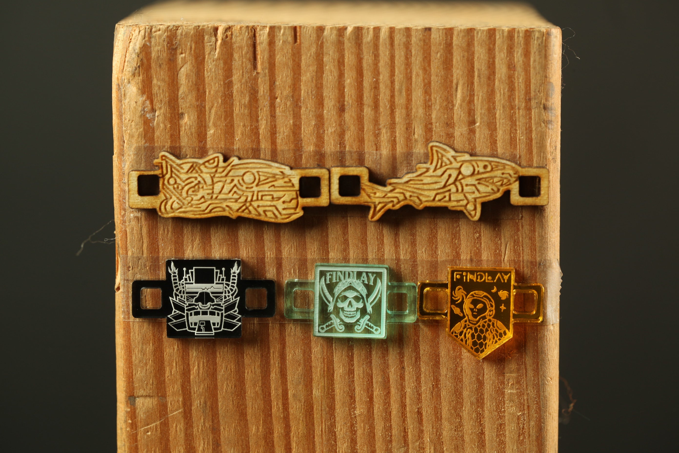 three different wooden pieces with various designs and colors, including a skull and crossbones, a fish, and a shield with the word "FINLAND".