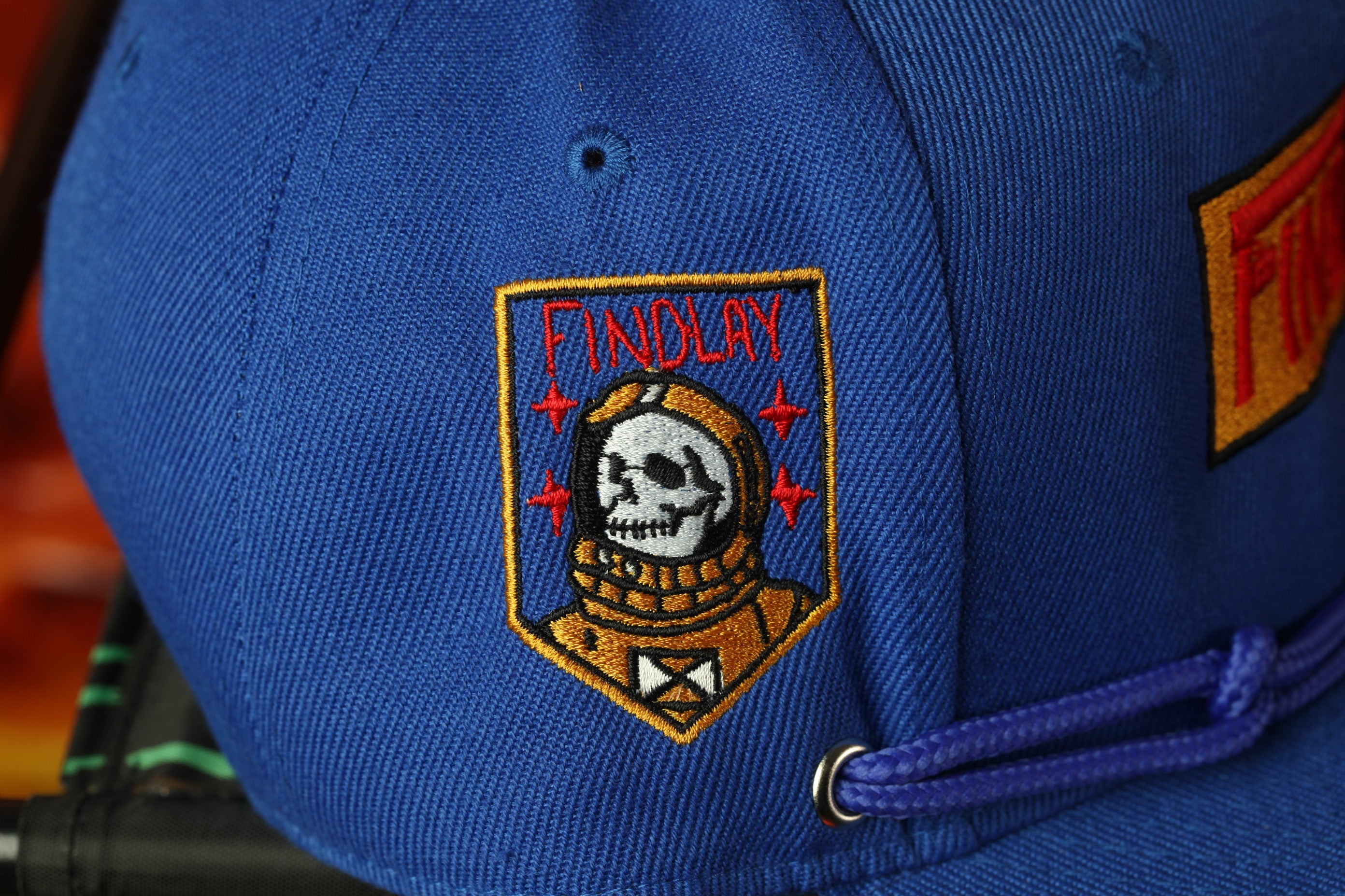 A close-up view of a blue baseball cap with a skull and crossbones design on the front.