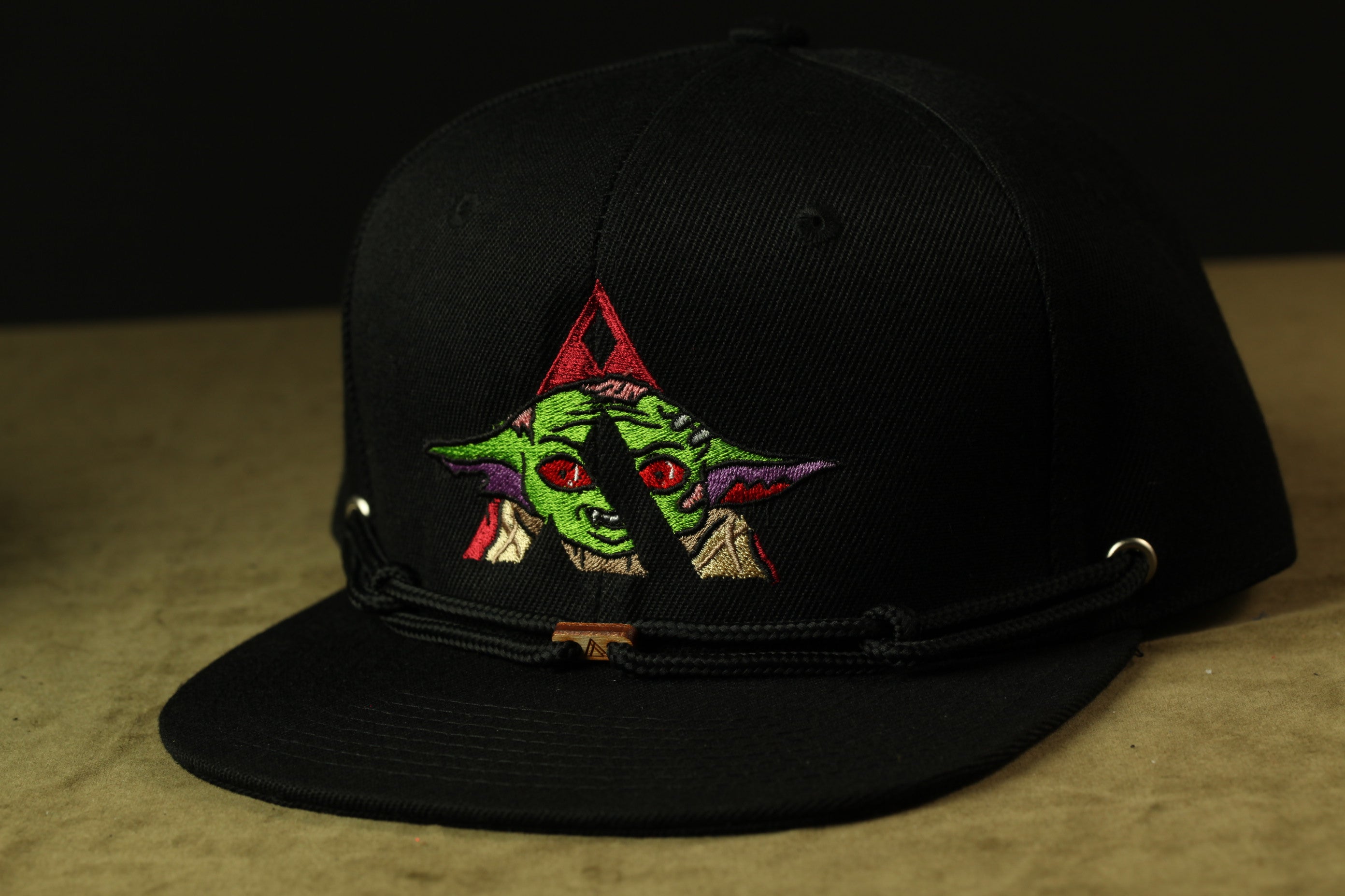 A black baseball cap with a colorful graphic of a character resembling Yoda from the Star Wars franchise.