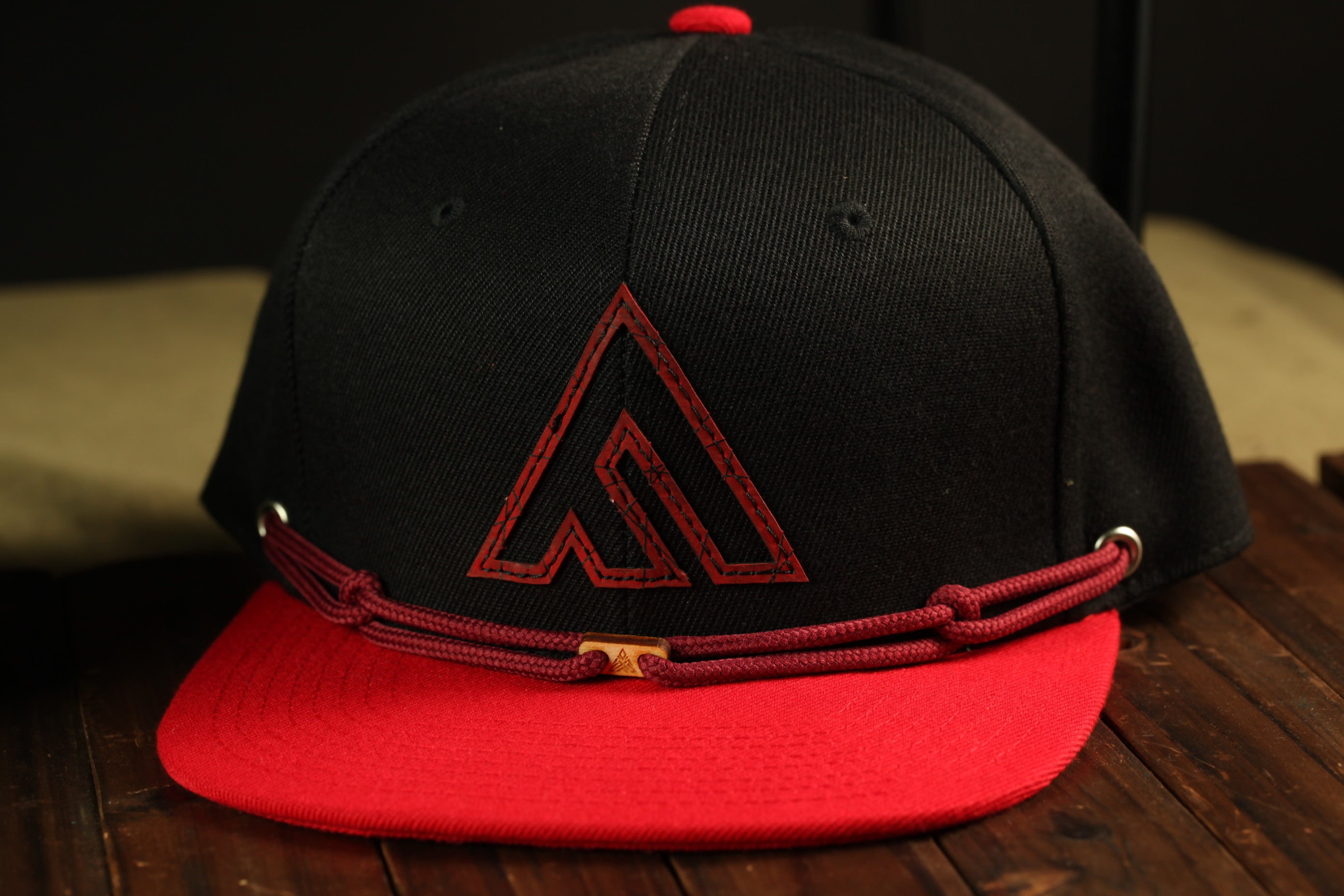 A black baseball cap with a red logo on the front, placed on a wooden surface.