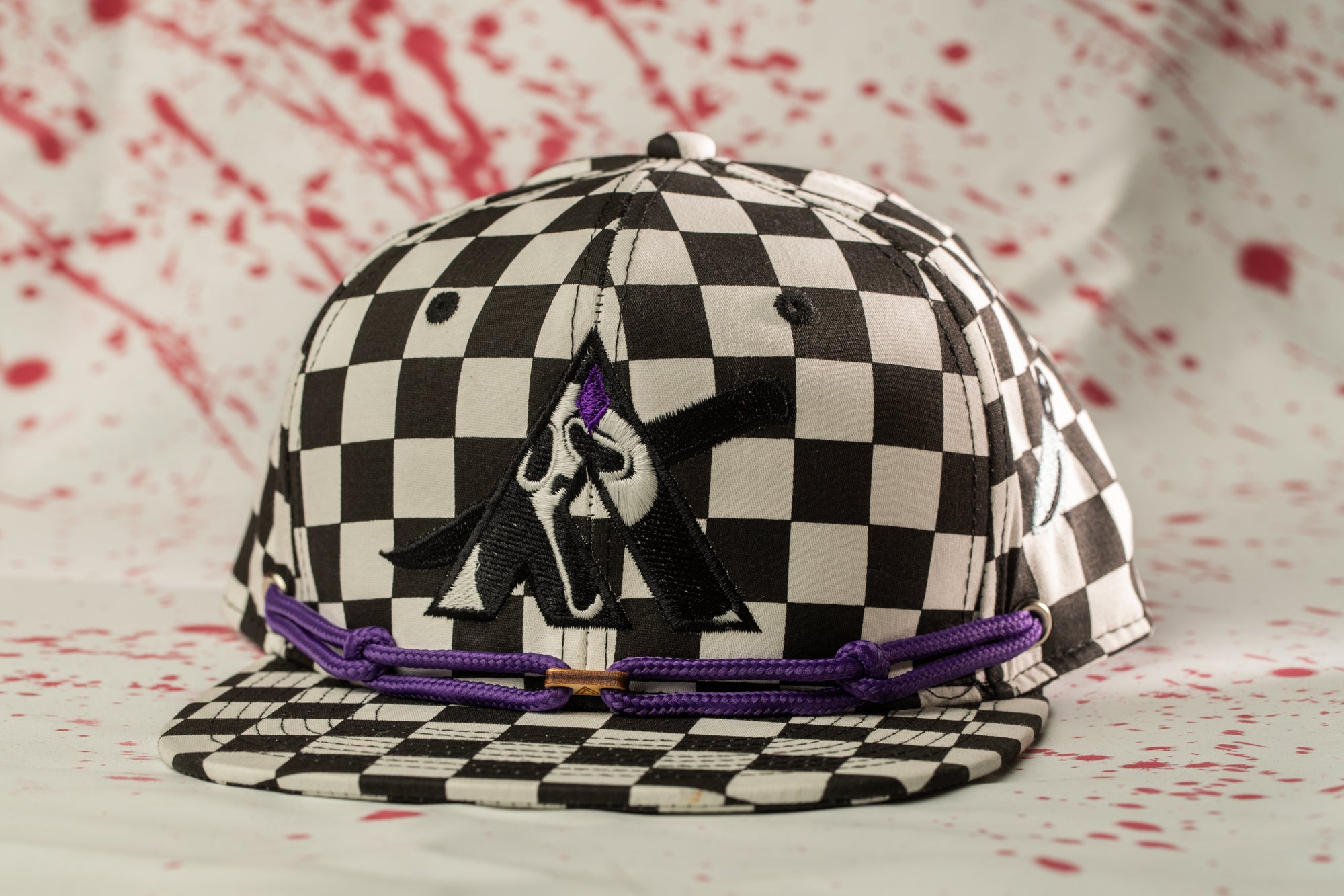 A black and white checkered baseball cap with a purple string and a graphic design on the front.