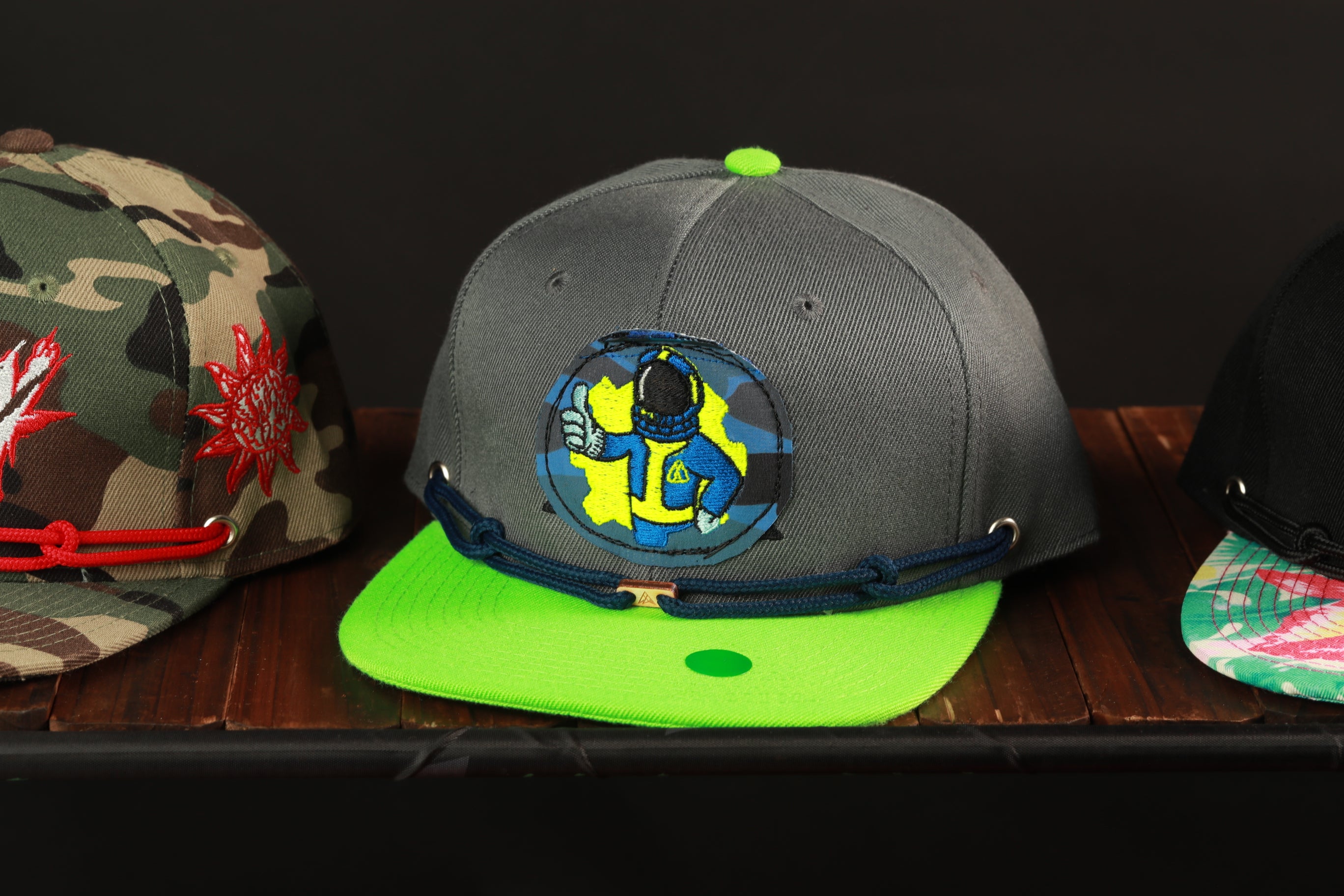 Three baseball caps are displayed on a wooden surface, each with different designs and colors.