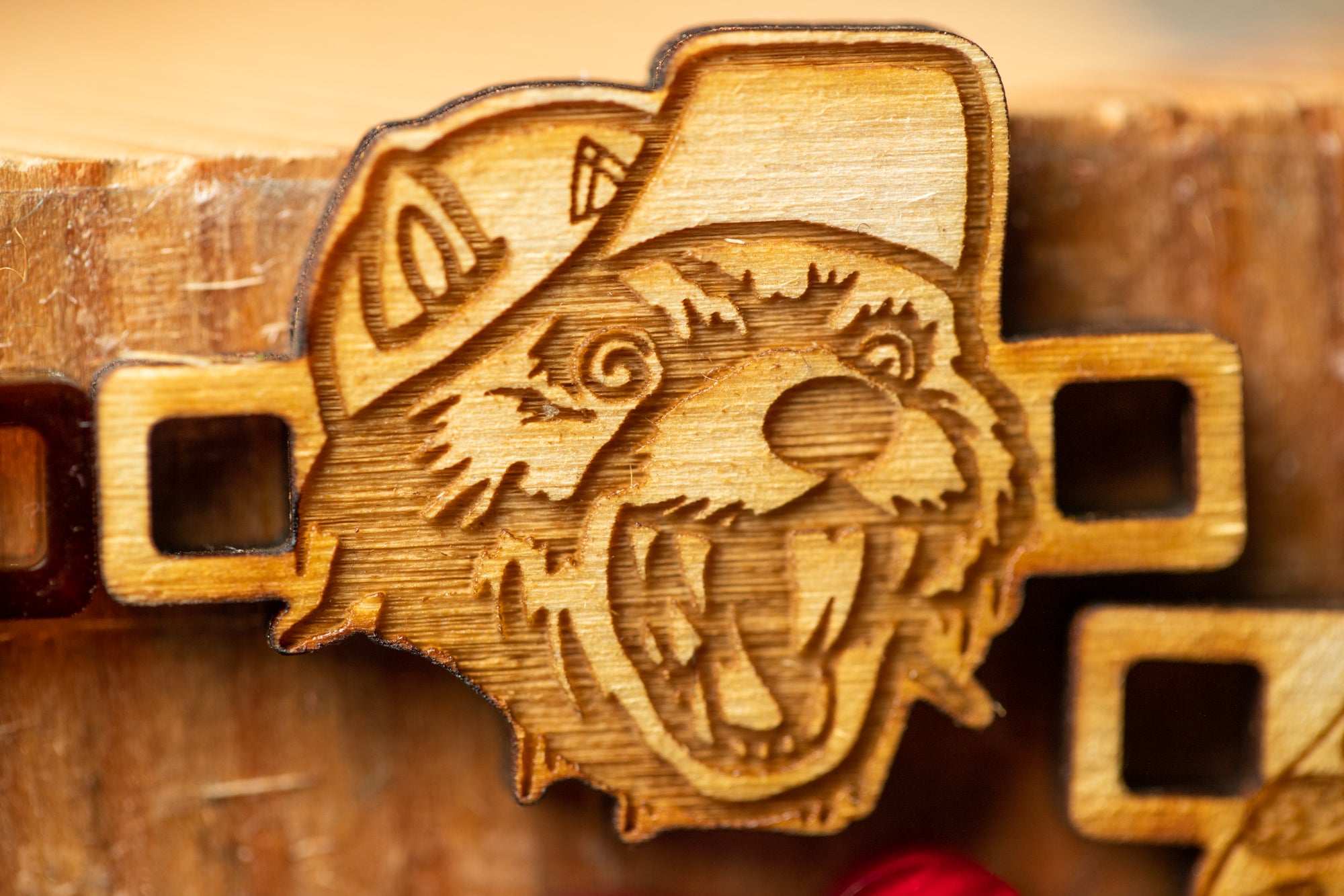 A wooden object with a carved design depicting a smiling, laughing bear wearing a baseball cap.