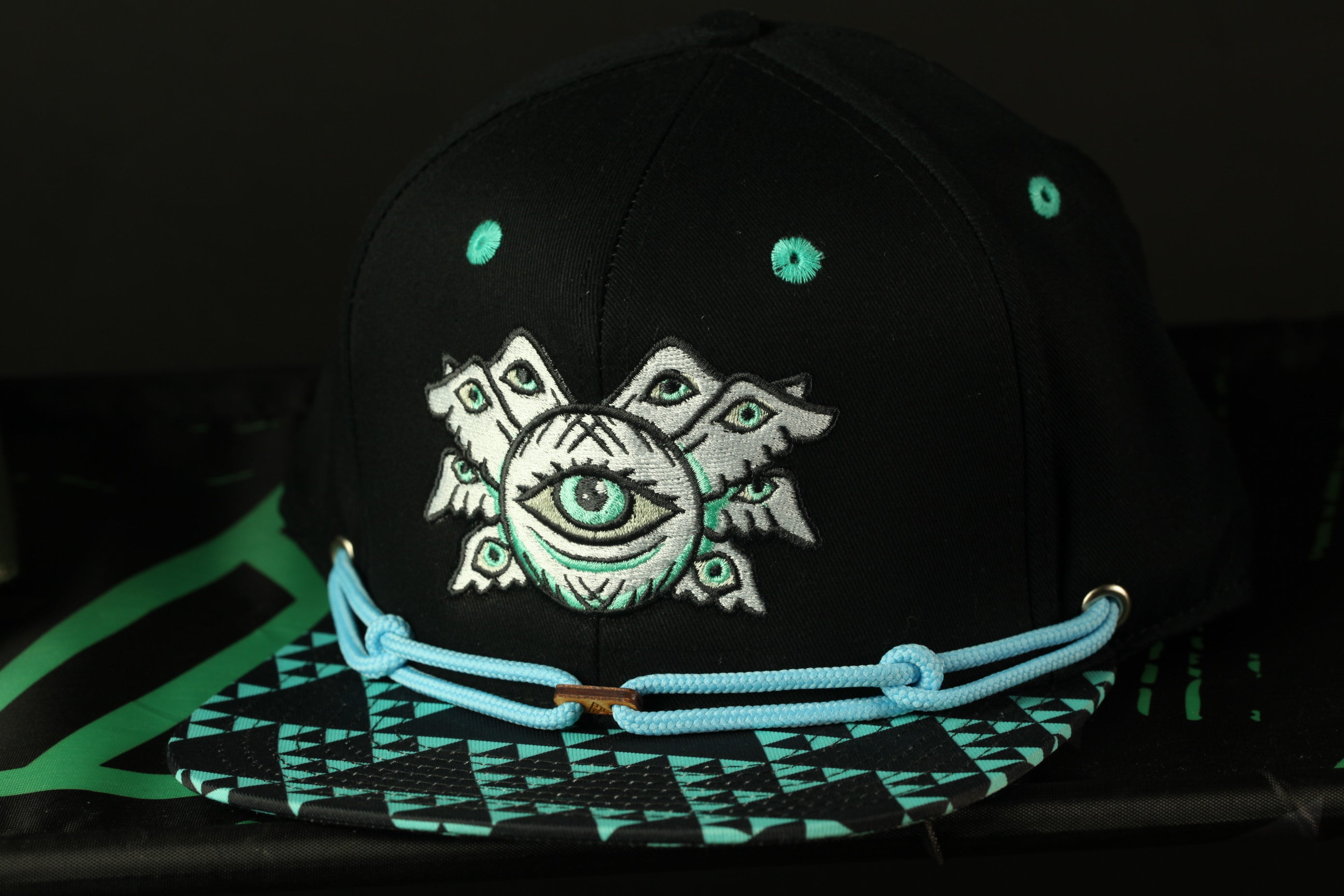 A black baseball cap with a unique eye design and a geometric pattern on the brim.