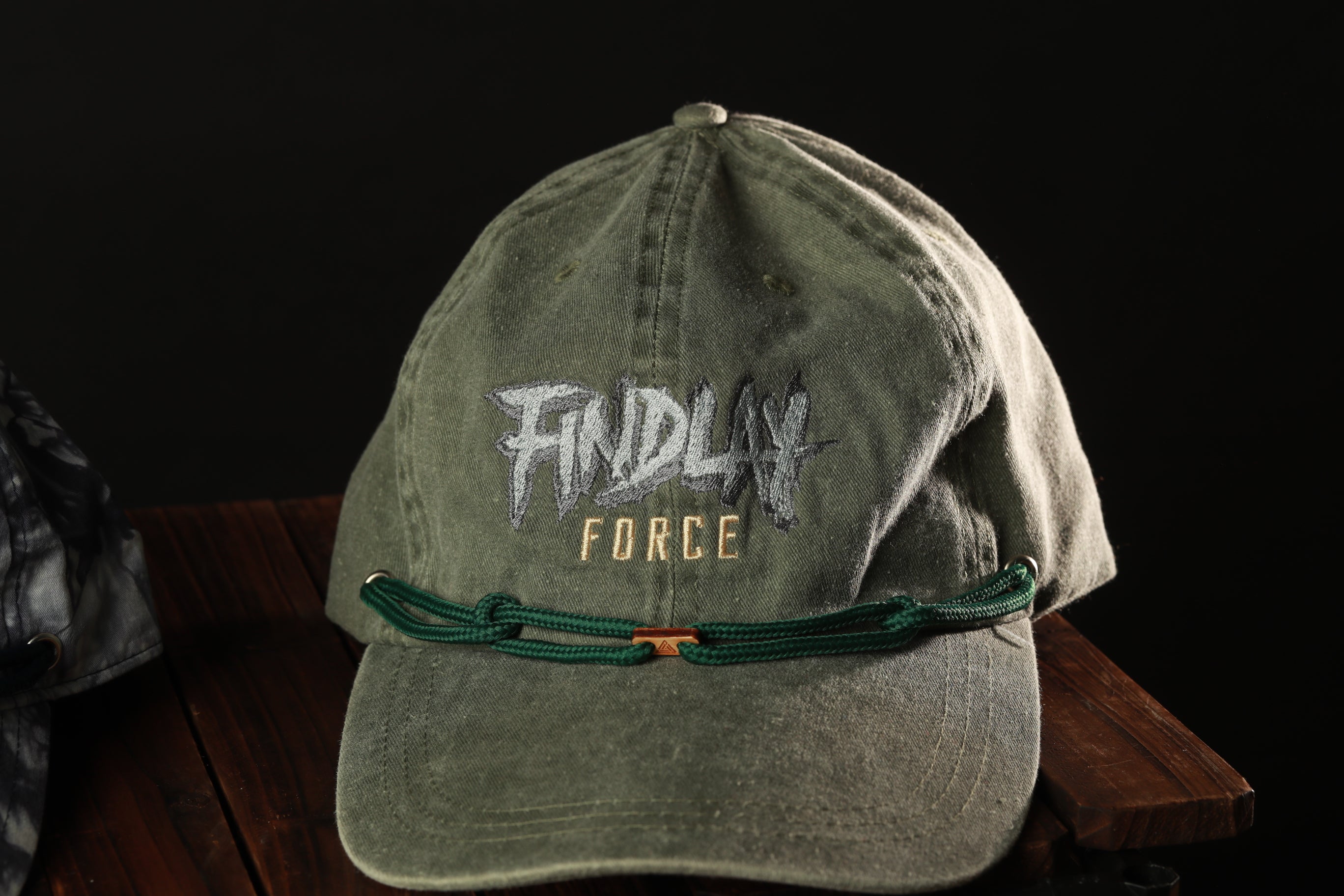A green baseball cap with the text "FINDL" and "FORCE" printed on it, along with a green string or strap.
