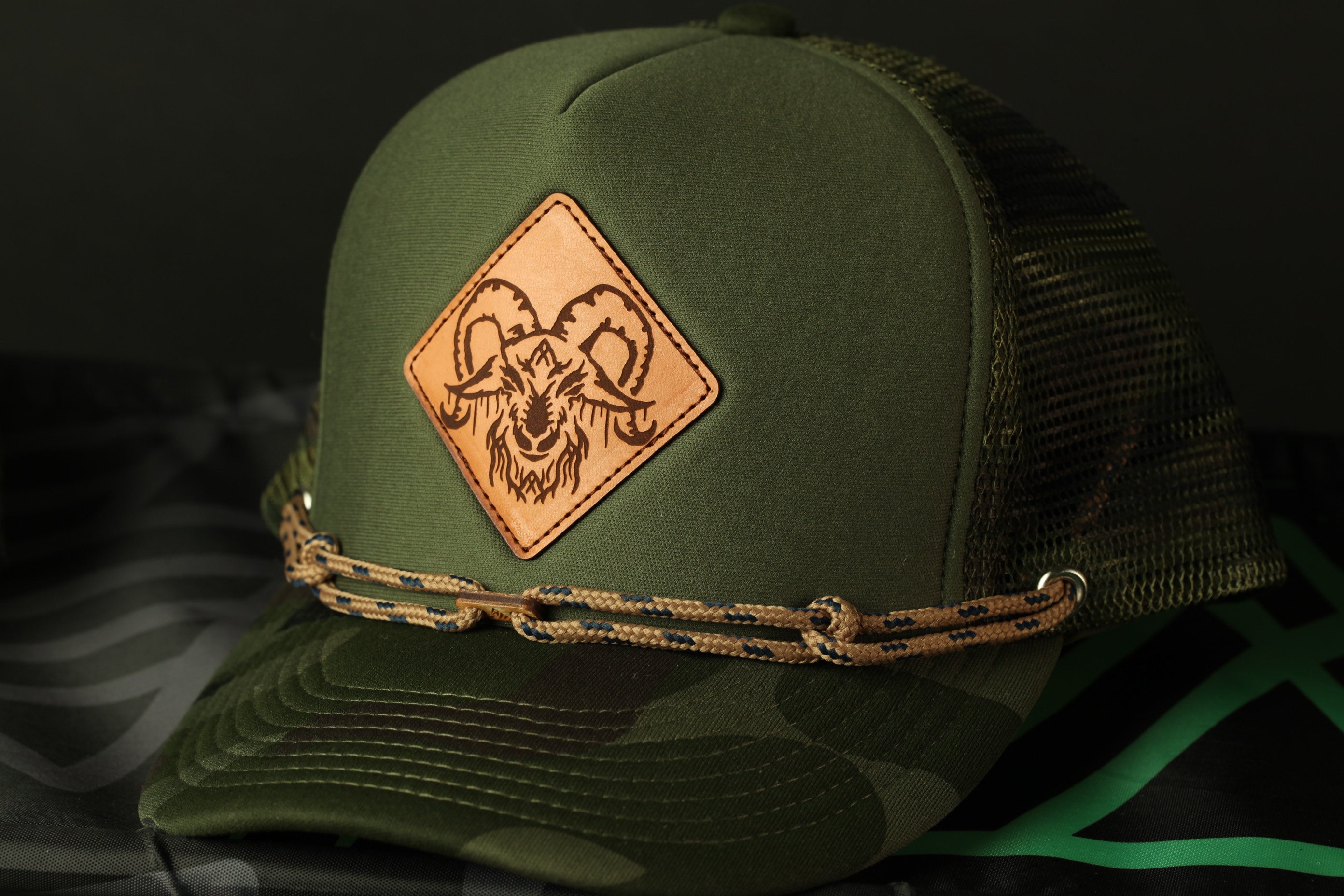 A green baseball cap with a leather patch featuring a goat's face design.