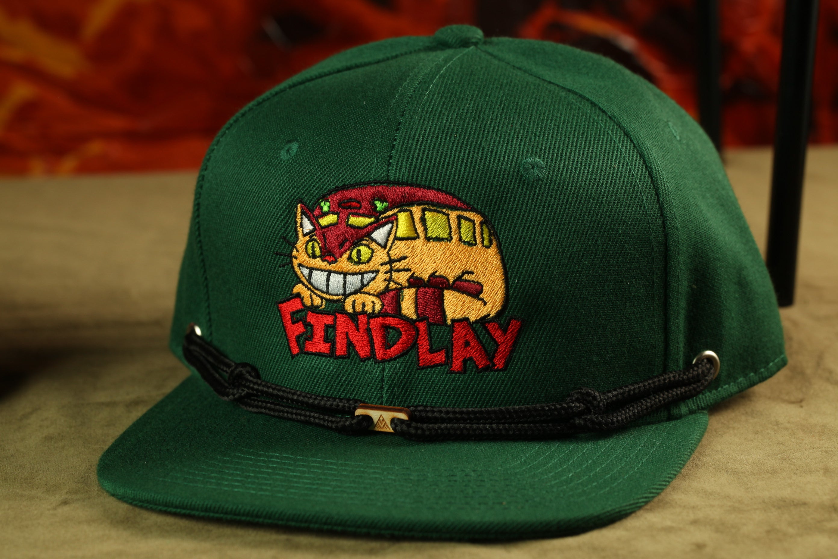 A green baseball cap with a cat embroidered on it, featuring the word "FINDLAY" on the front.