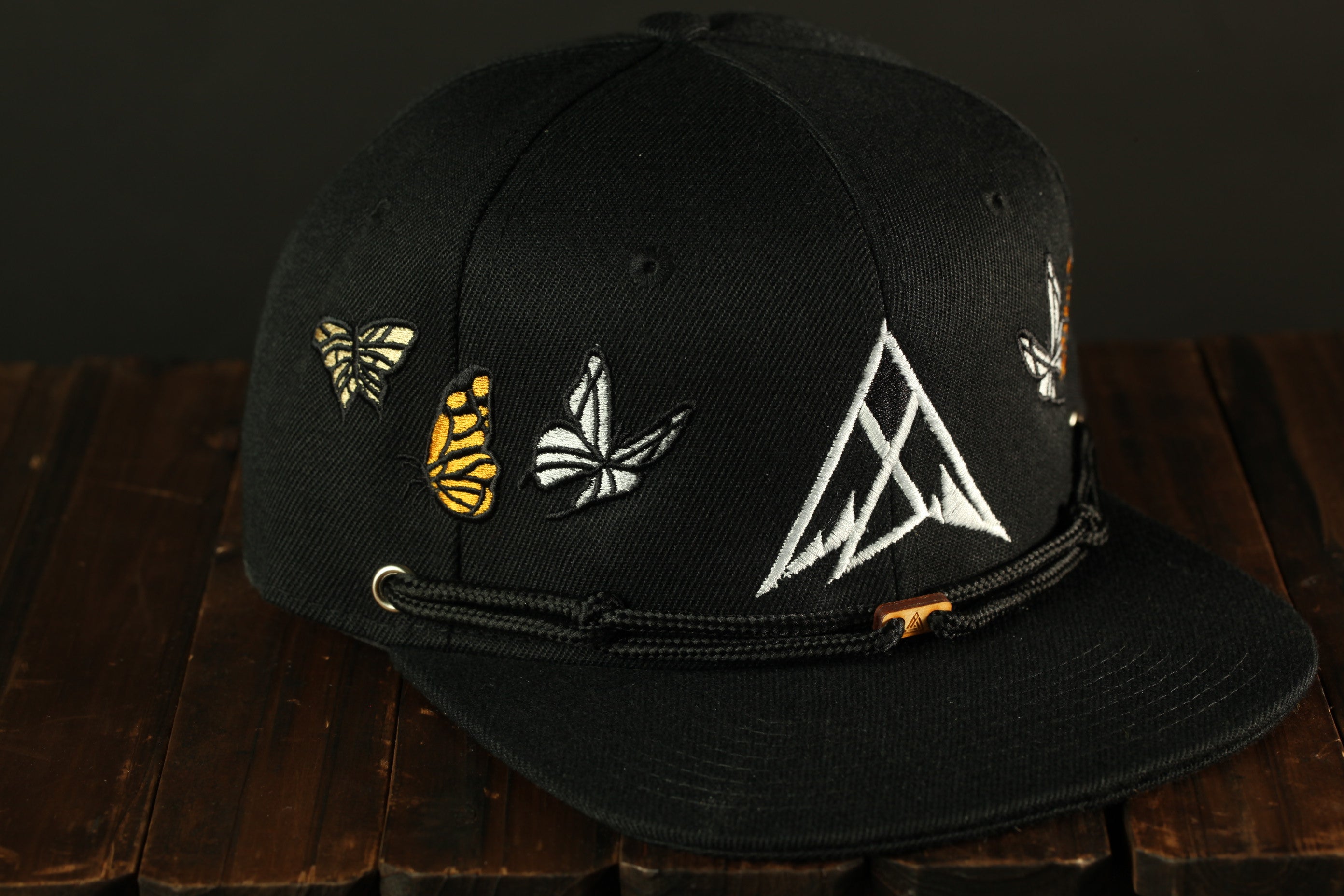 A black baseball cap with a white triangle design and several butterflies embroidered on the front.