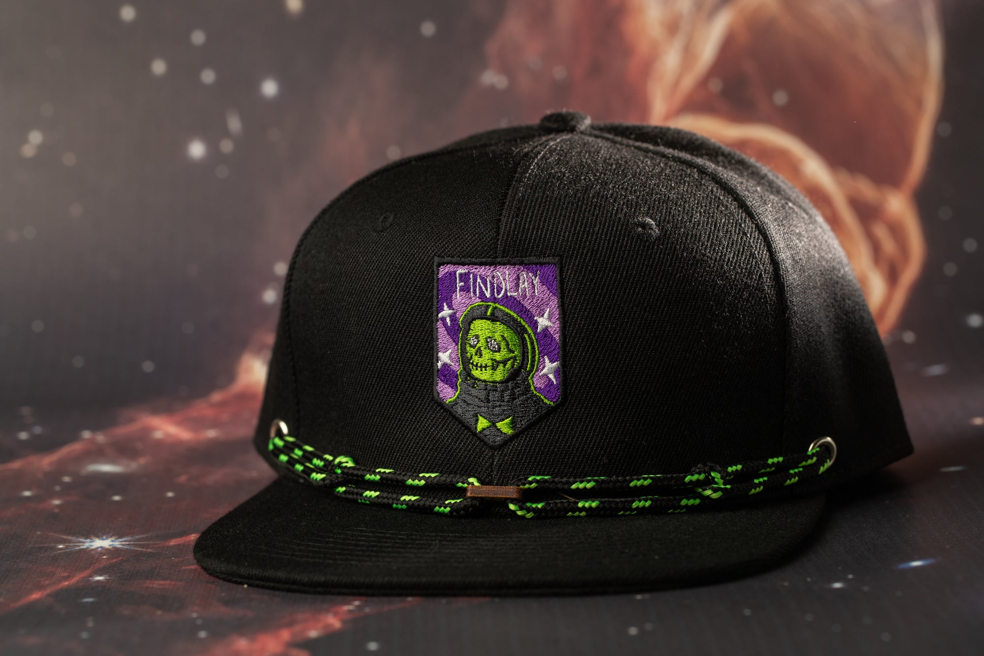 A black baseball cap with a green and purple patch featuring a skull and crossbones design, along with a green string or strap.