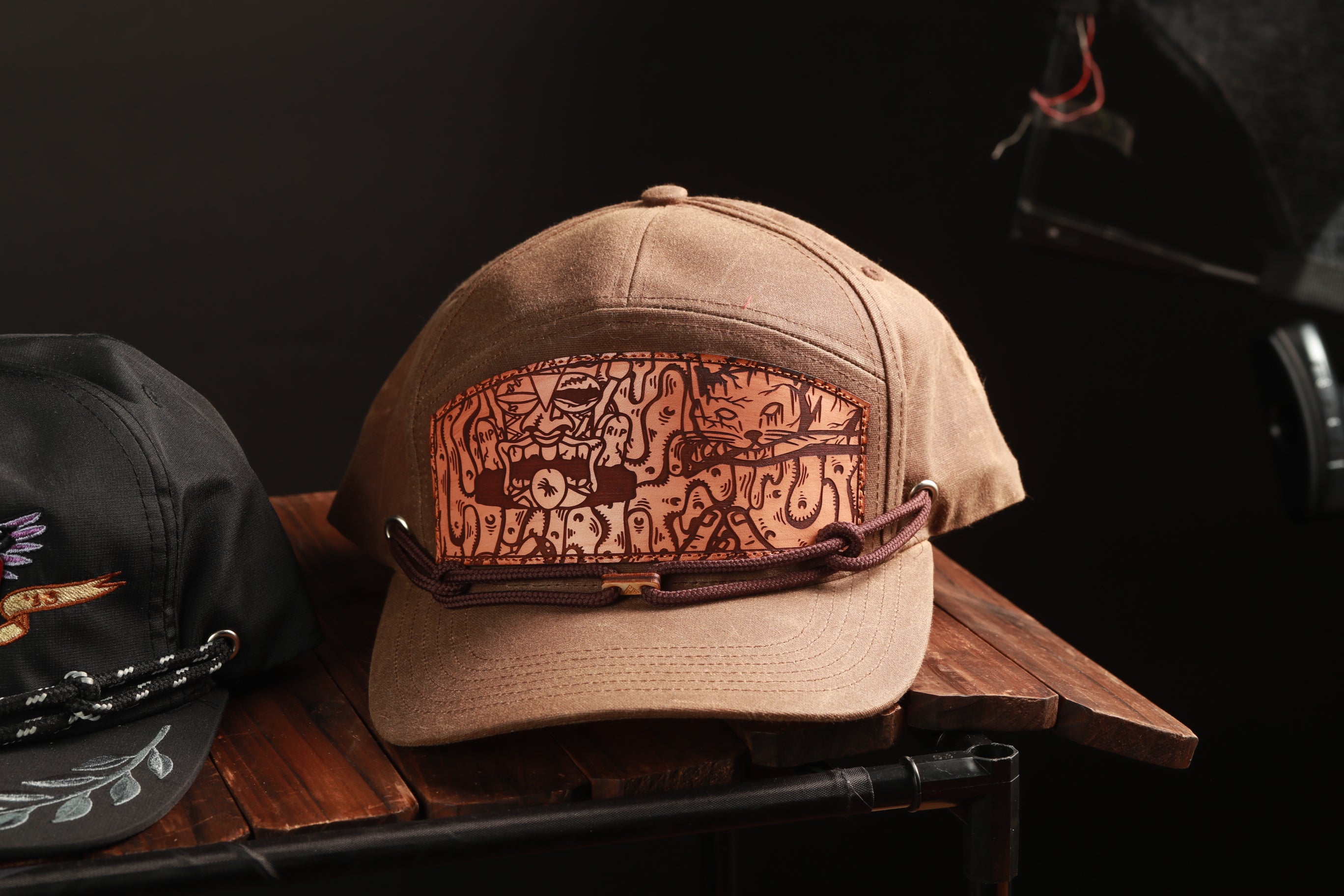 A tan baseball cap with a unique, hand-drawn design on the front, placed on a wooden surface.
