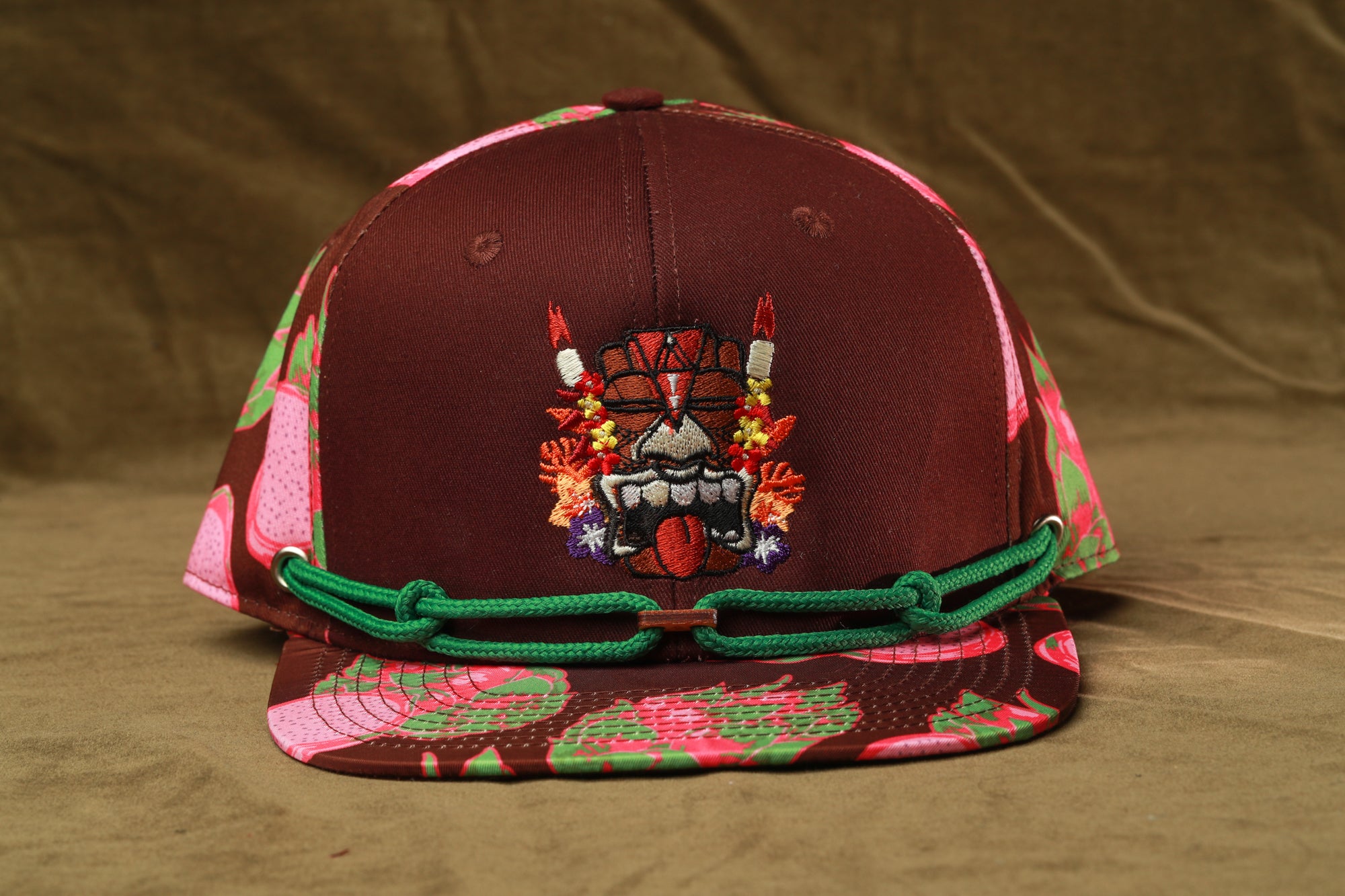 A brown baseball cap with a floral pattern and a graphic design on the front.