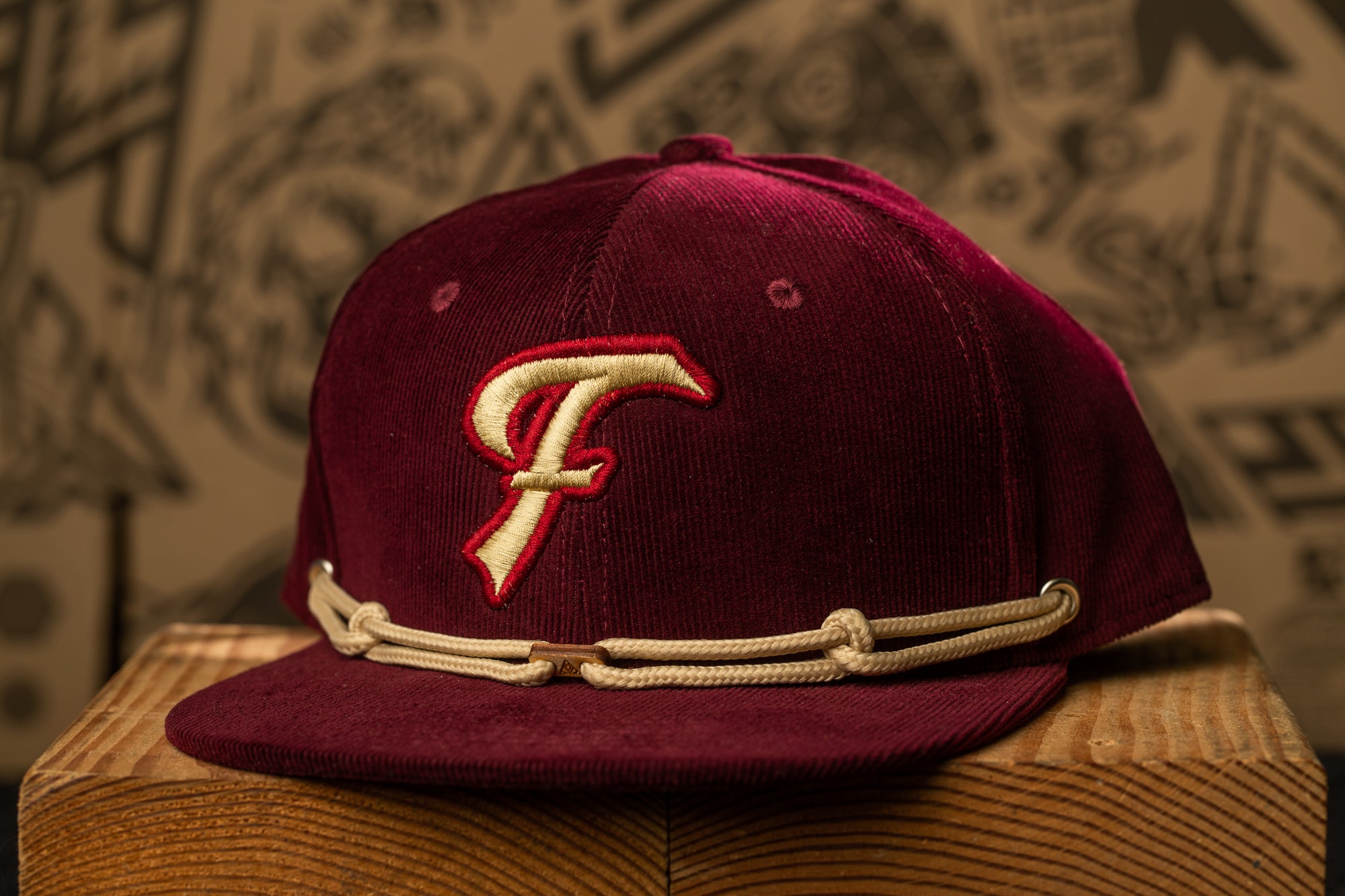 A burgundy baseball cap with a white "F" logo on the front, sitting on a wooden surface.