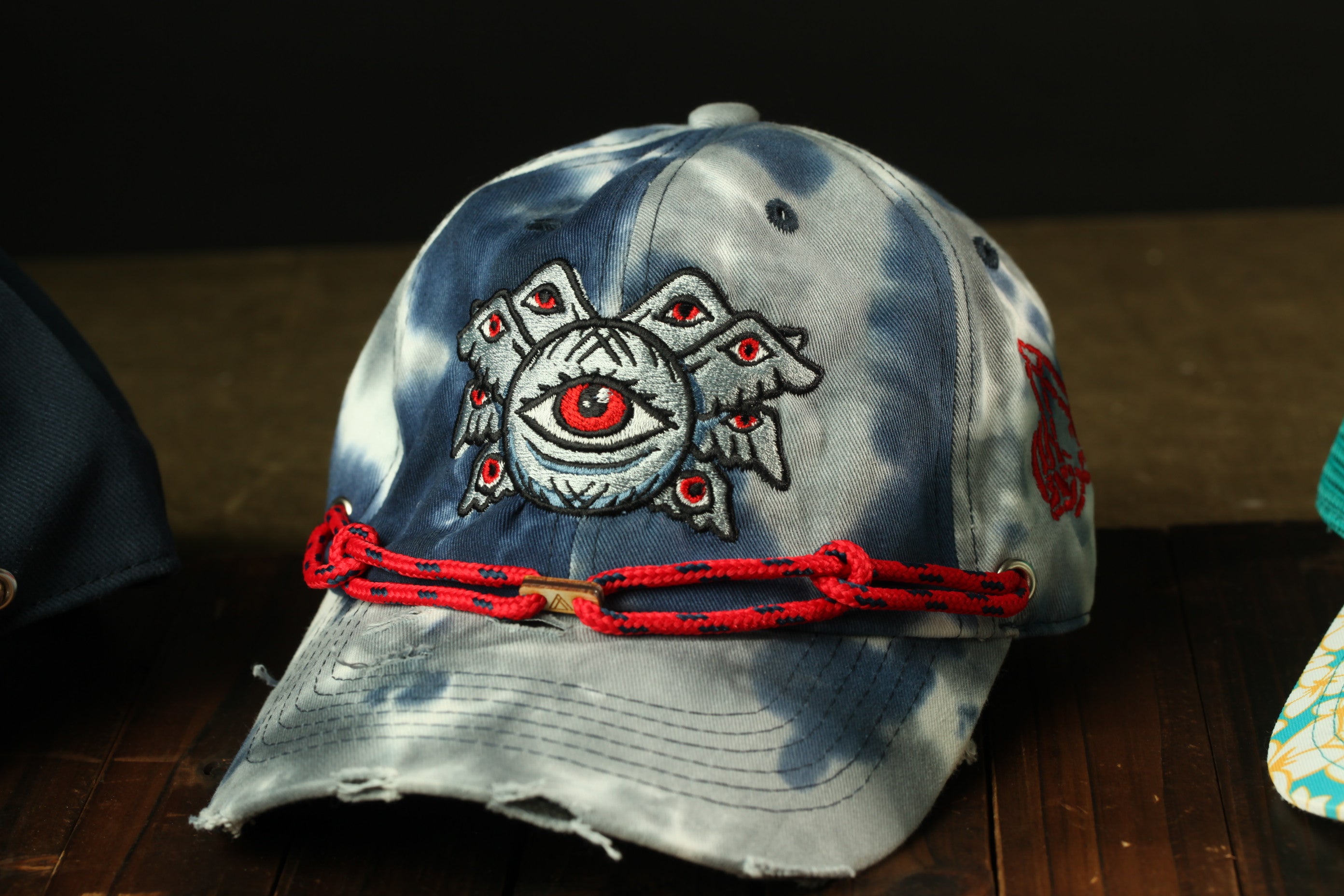A tie-dye baseball cap with an eye design and a red string around the brim.