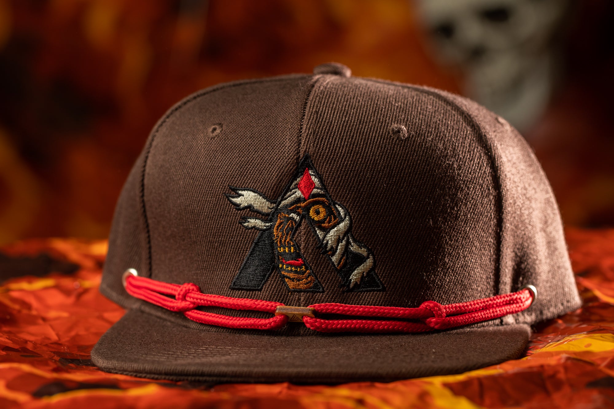 A brown baseball cap with a red string and an embroidered logo on the front.