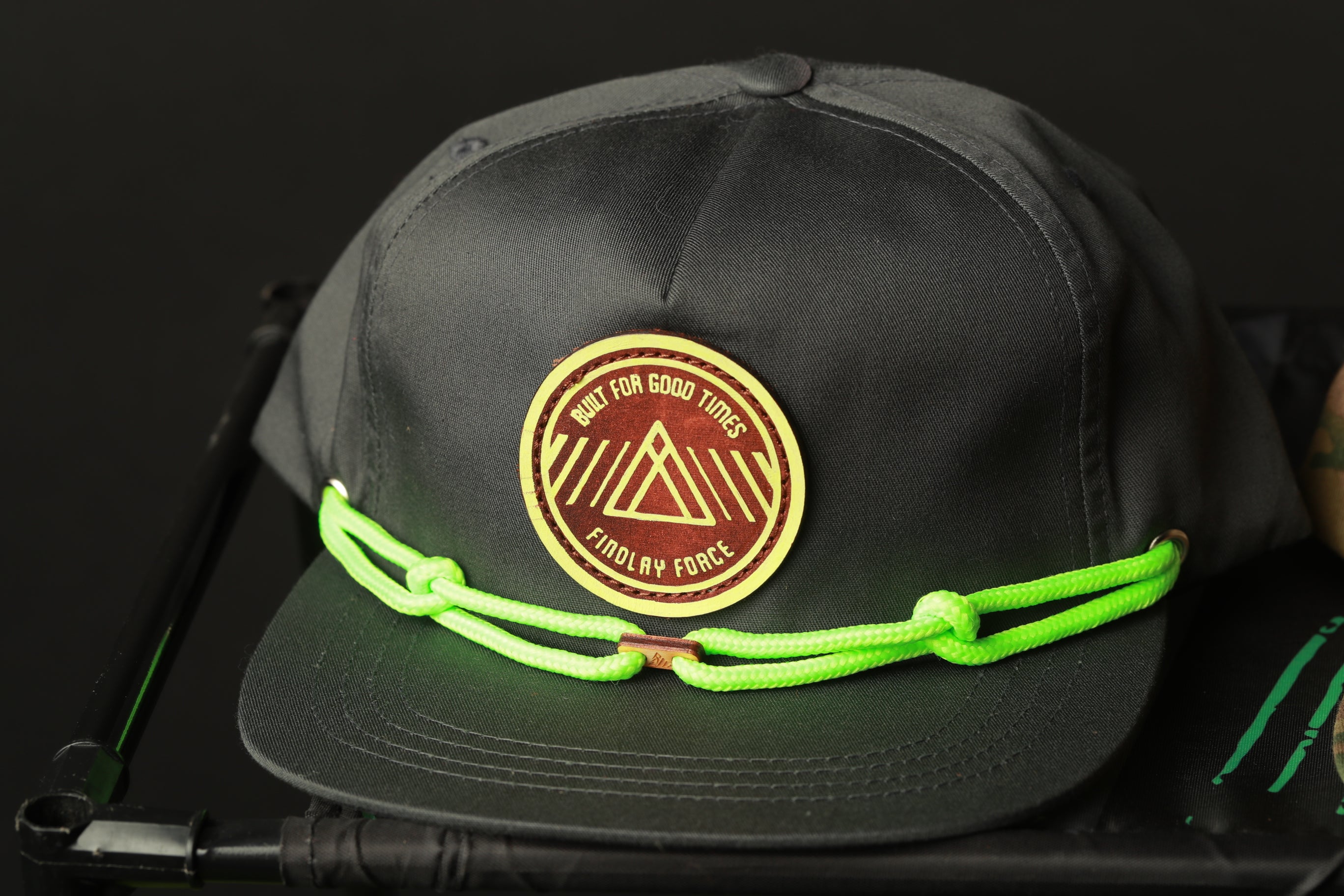 A black baseball cap with a yellow and red patch on the front, featuring a triangle design and the text "BUILD FOR GOOD TIMES FIND MY FORCE" written on it.