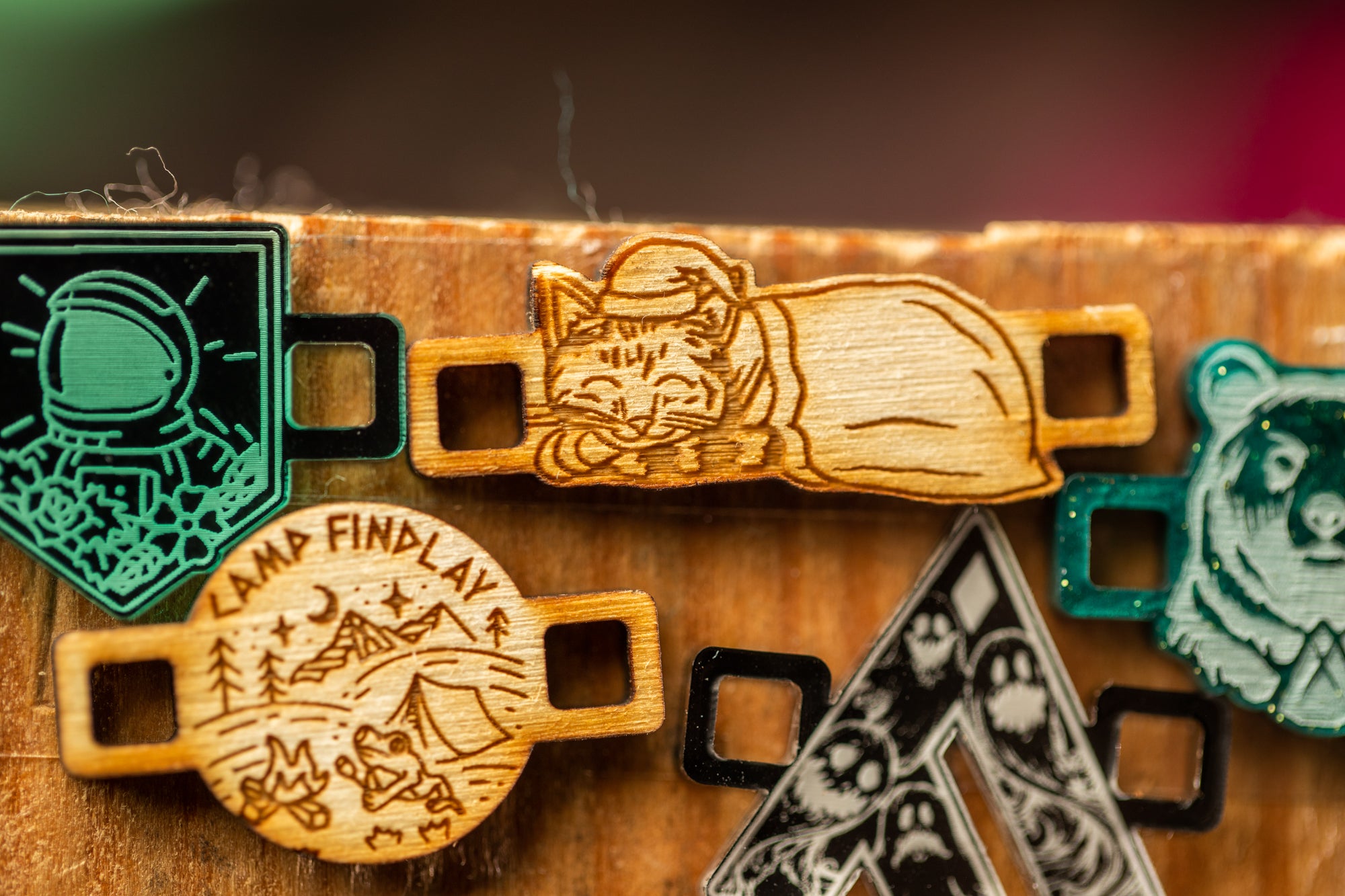 a collection of wooden objects, including a wooden charm with a cat design, a wooden charm with a space theme design, and a wooden charm with a bear design.