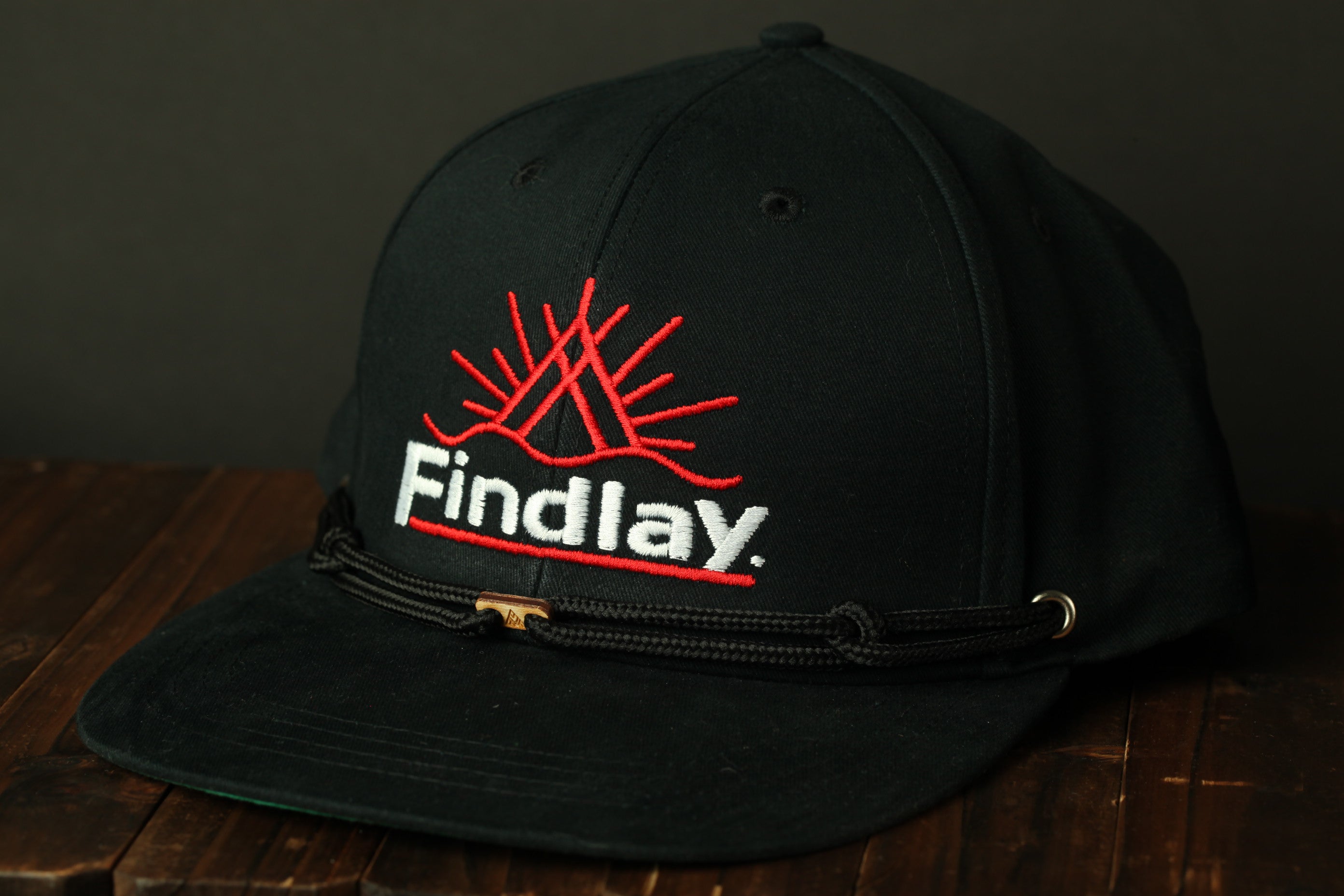 A black baseball cap with a red sun design and the word "Findlay" printed on it.