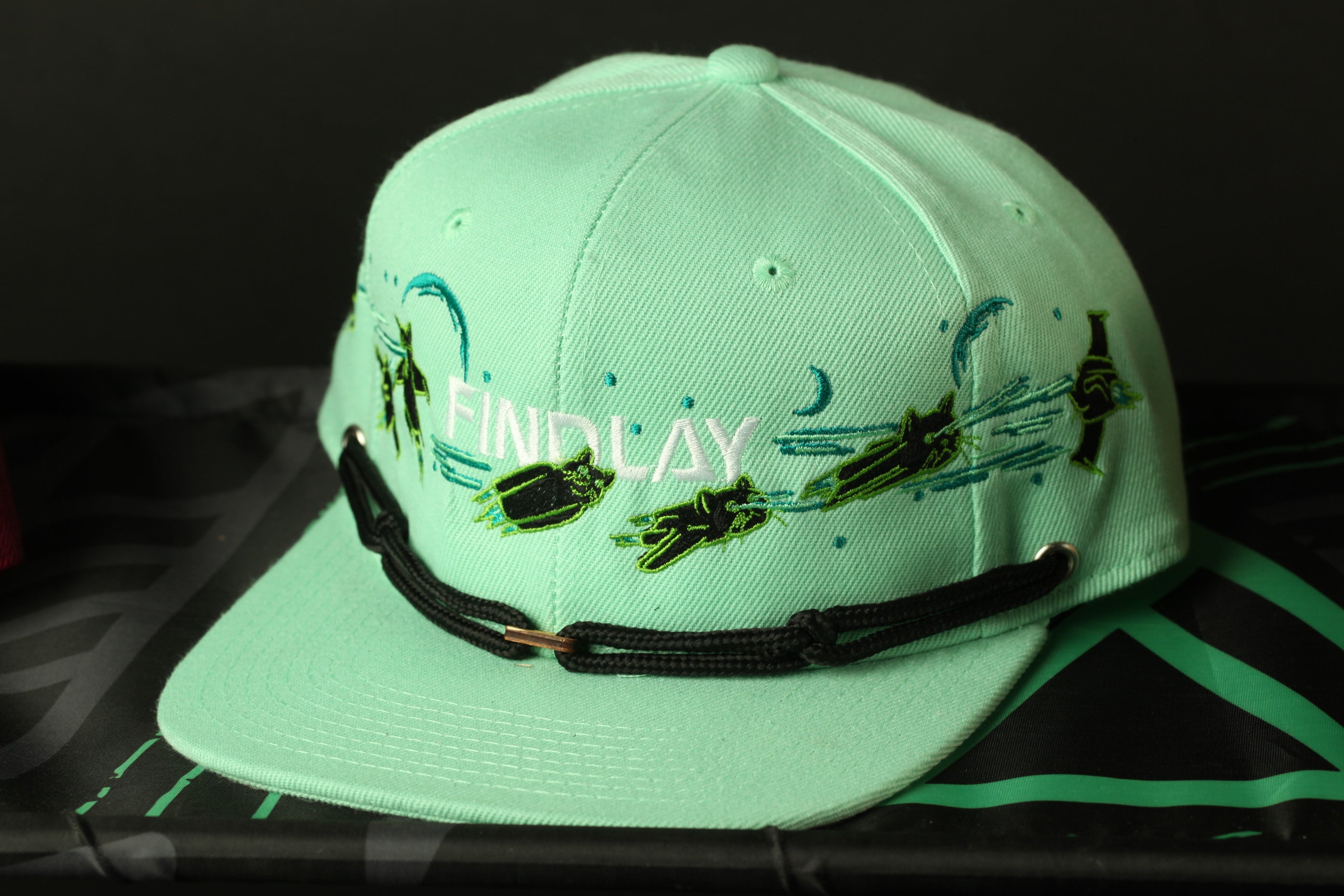 A mint green baseball cap with a black strap and the word "FINDlay" printed on it.