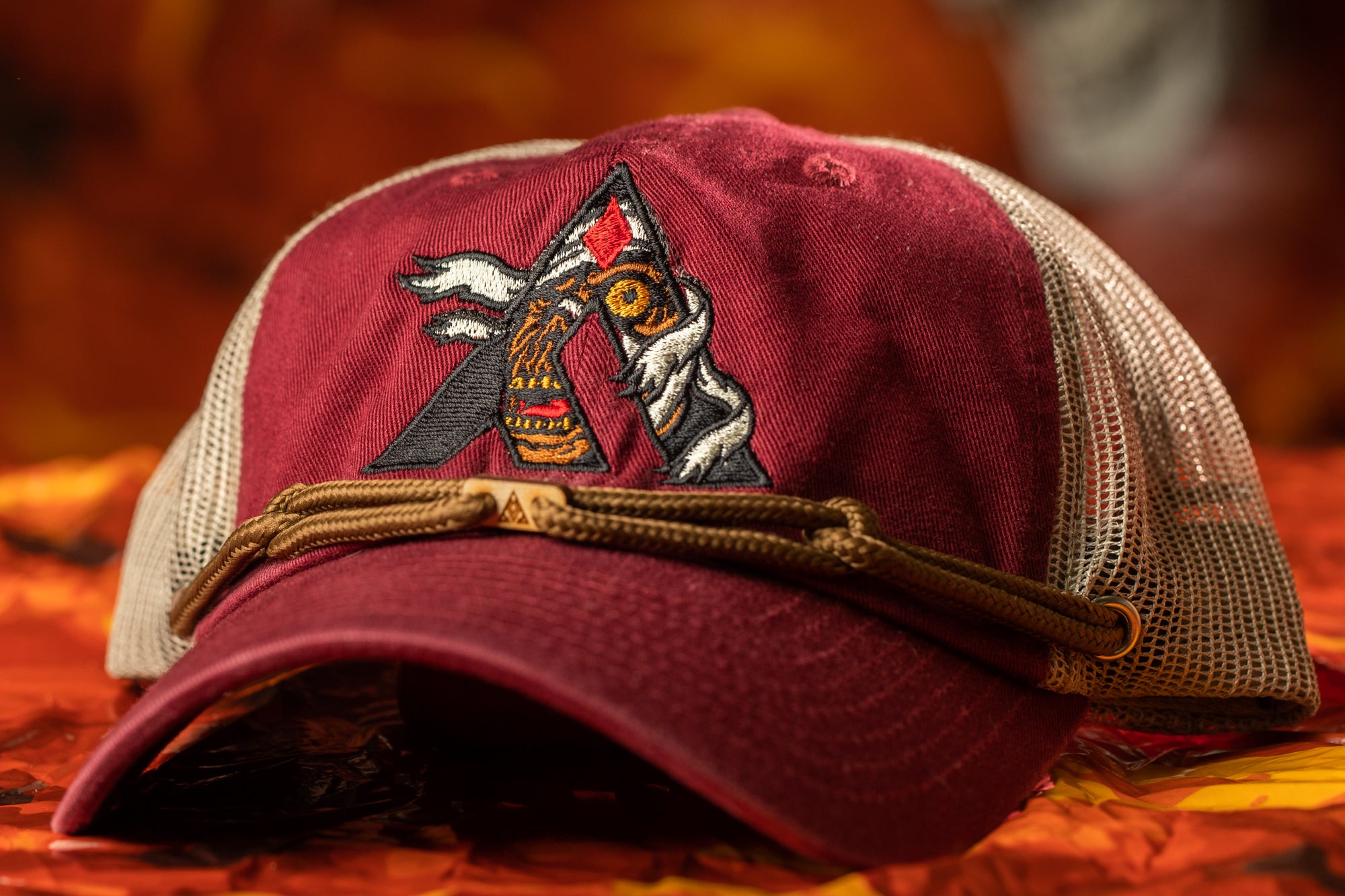 A maroon baseball cap with a mesh panel and a decorative embroidered logo on the front.
