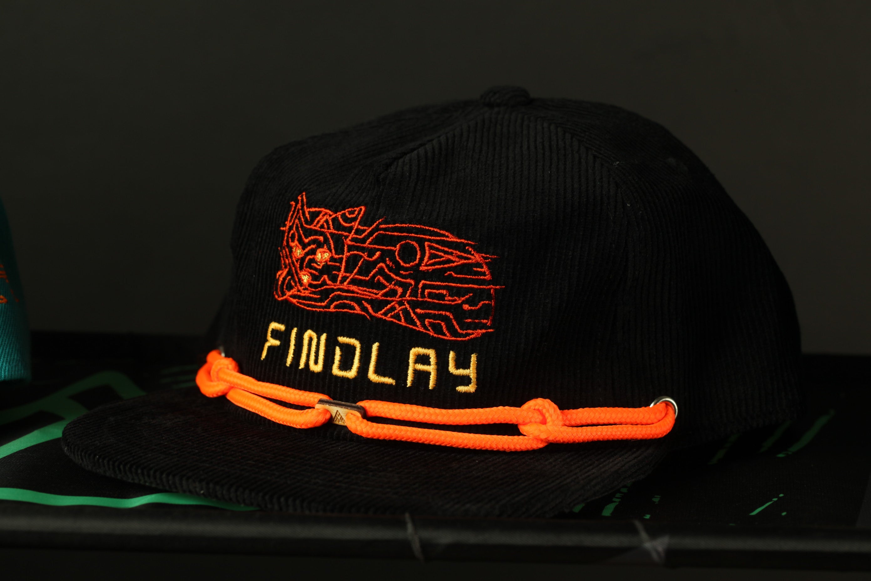 A black baseball cap with orange and yellow embroidered designs and the word "FINDLAY" printed on it.
