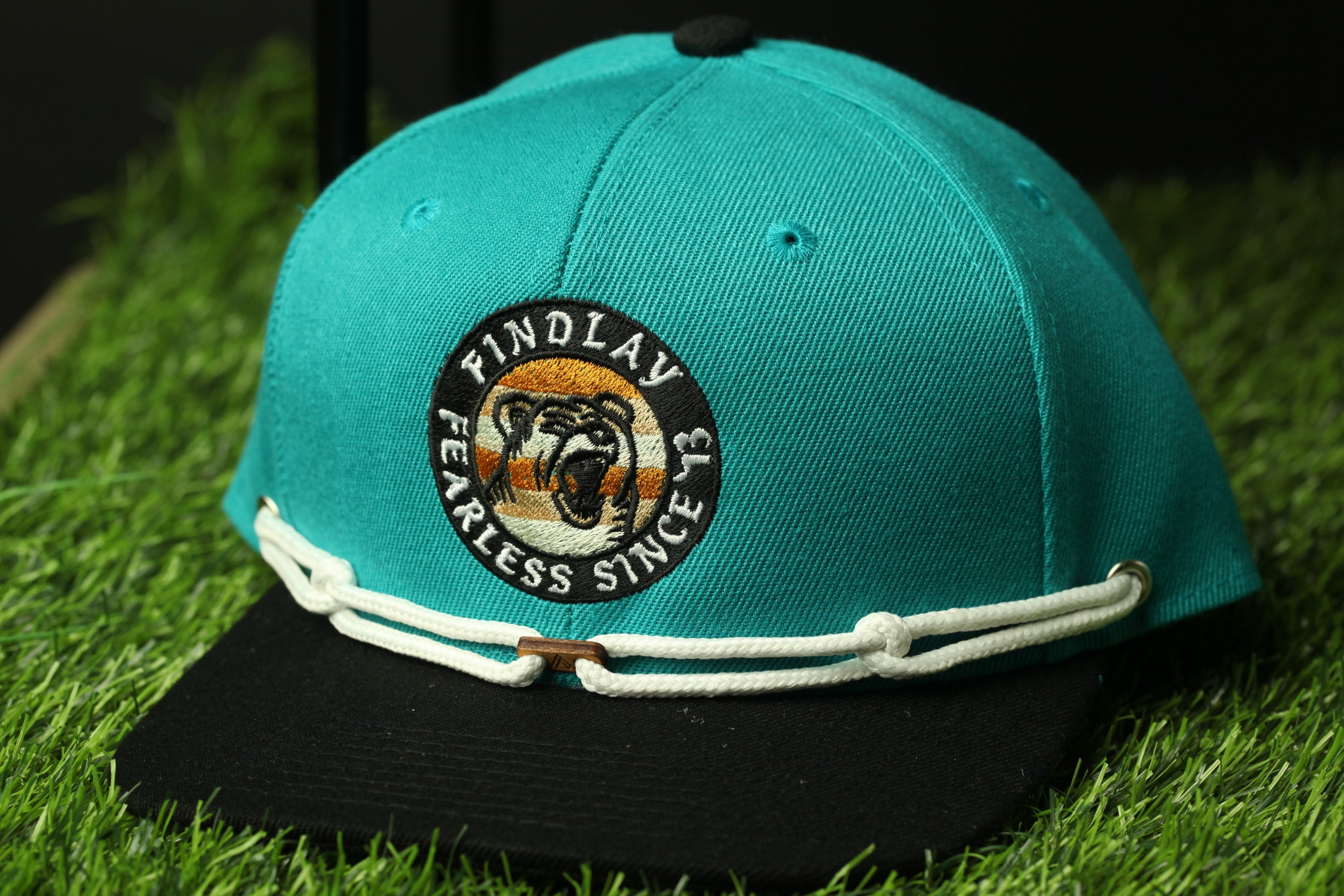 A turquoise baseball cap with a black brim and white lace trim, featuring a circular logo with a tiger's face and the text "FINDLAW FEARLESS SINCE 3".