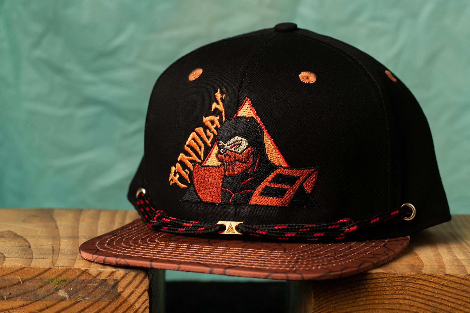 A black baseball cap with a graphic design on it, sitting on a wooden surface.