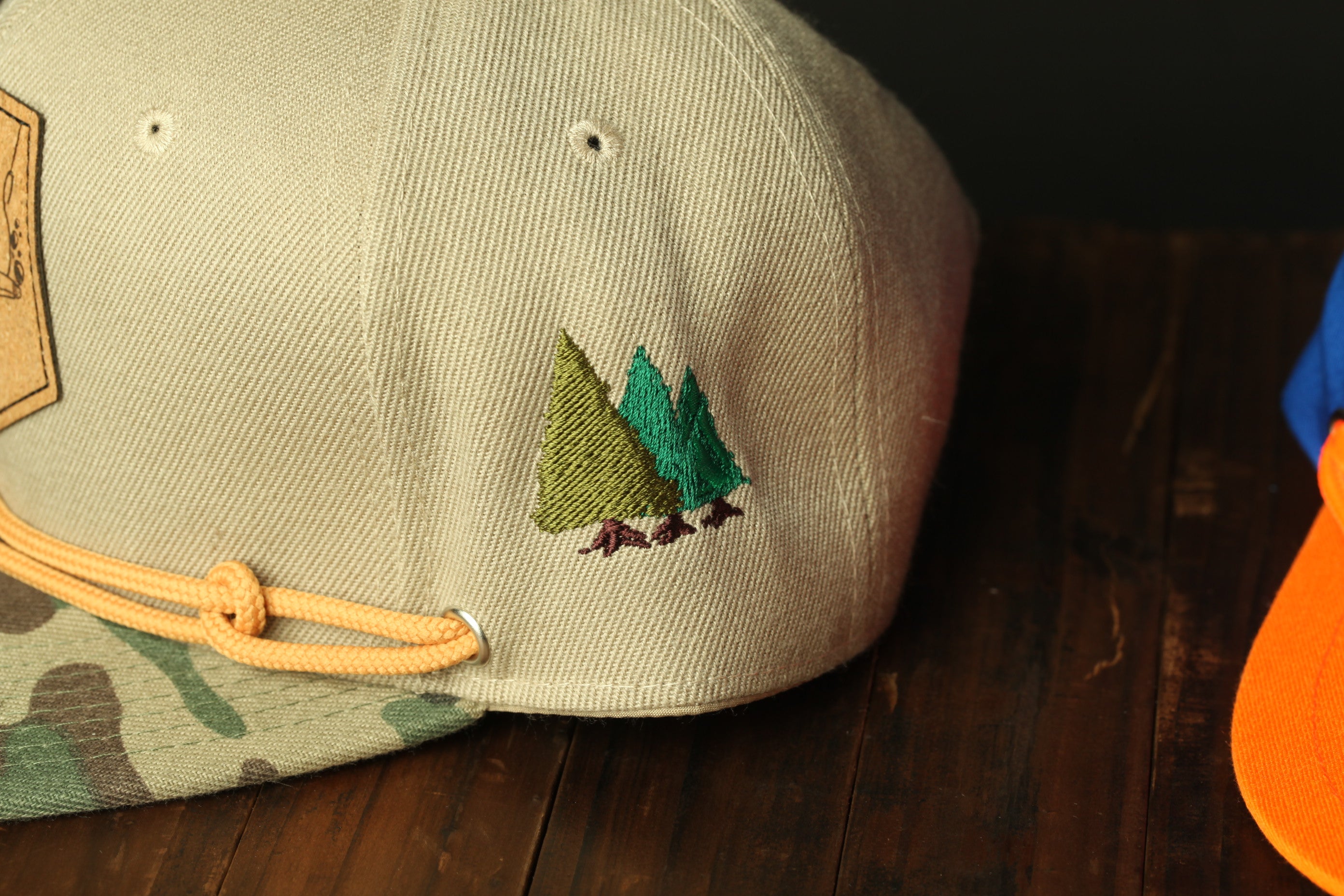 A beige baseball cap with a green tree embroidered on it, placed on a wooden surface.