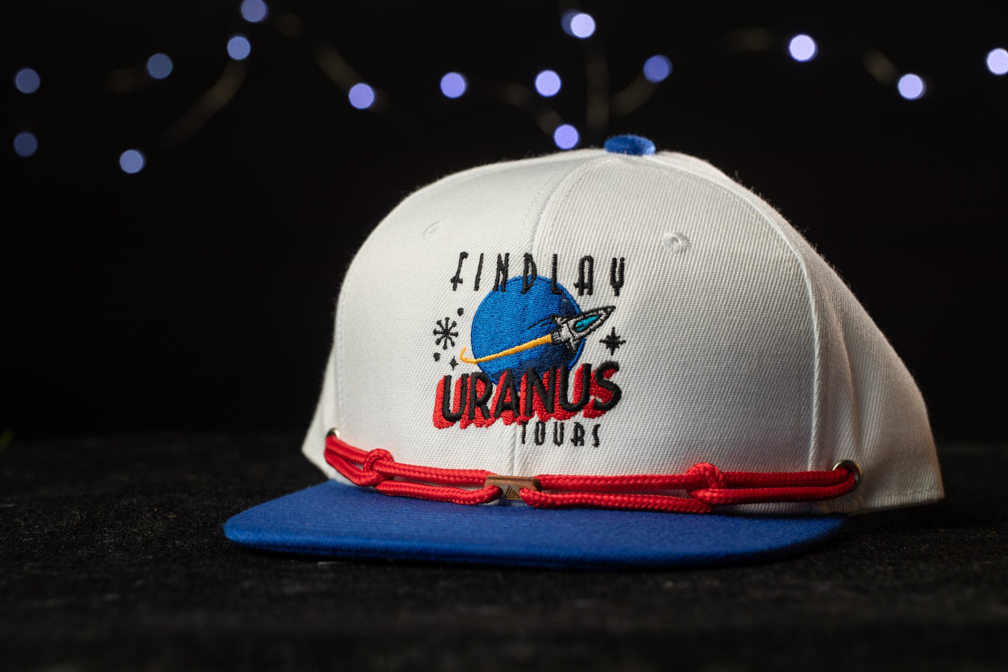 A white baseball cap with a blue brim and red string, featuring the text "FINDUY URAINUS TOUR" on the front.