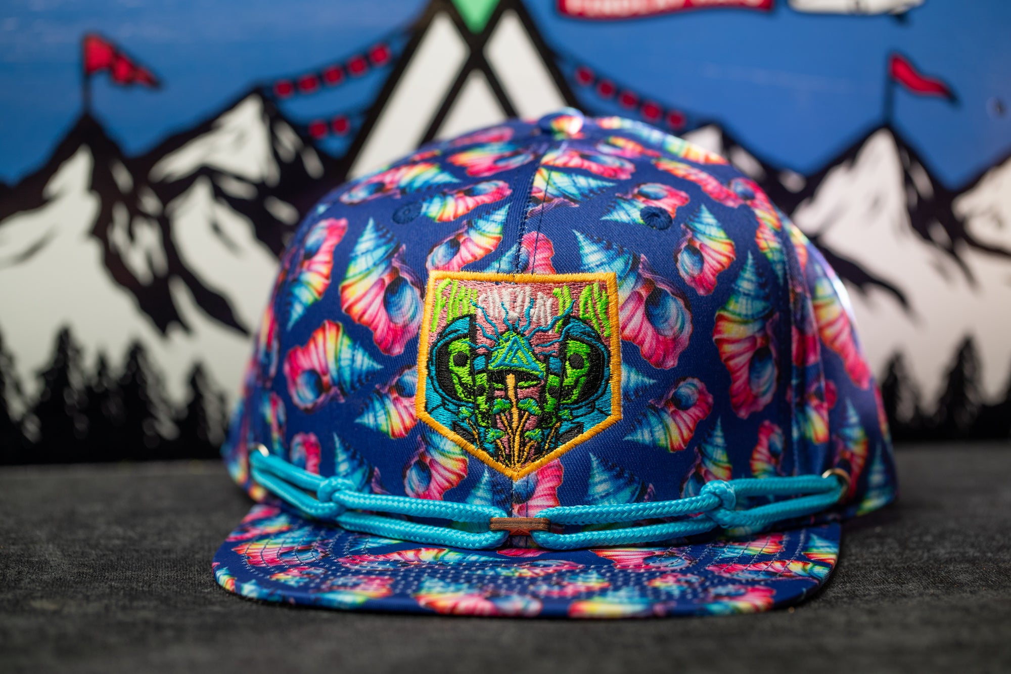 A colorful, patterned baseball cap with a unique design on the front, featuring a central patch with a mushroom-like creature and a green and yellow color scheme.