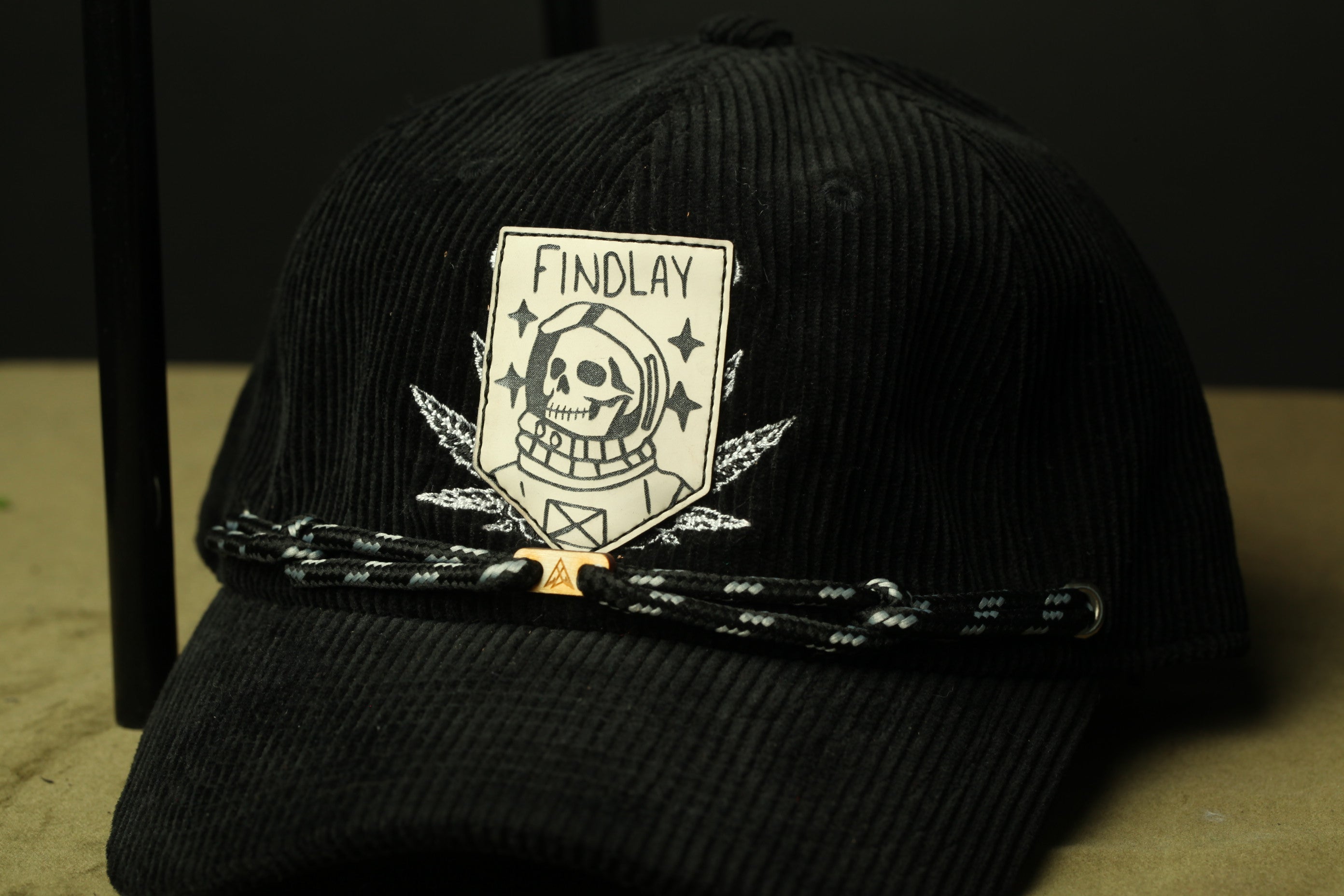 A black baseball cap with a white skull and crossbones design and the text "FINDLAY" printed on it.