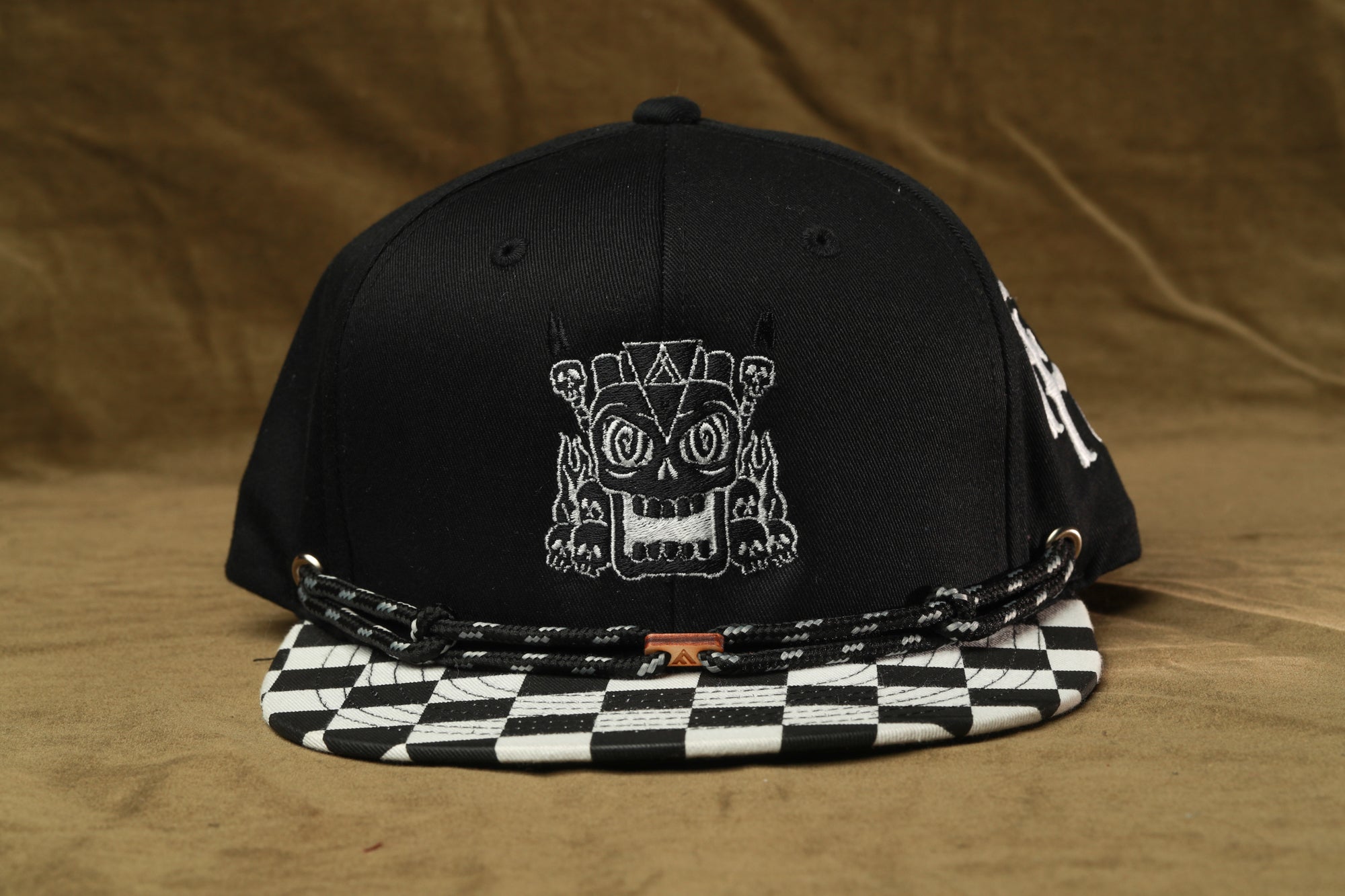 A black baseball cap with a white skull design on the front, placed on a checkered patterned part of the cap.