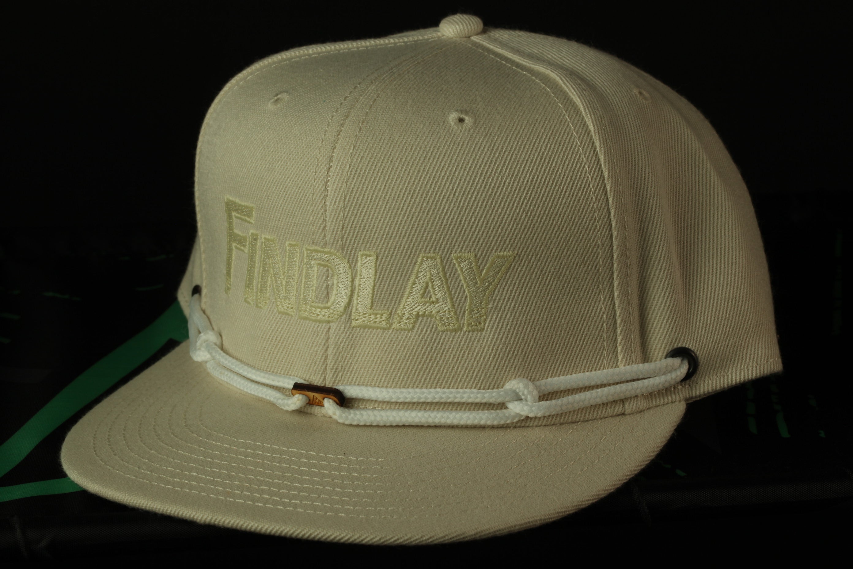 A beige baseball cap with the word "FINDlay" printed on it.