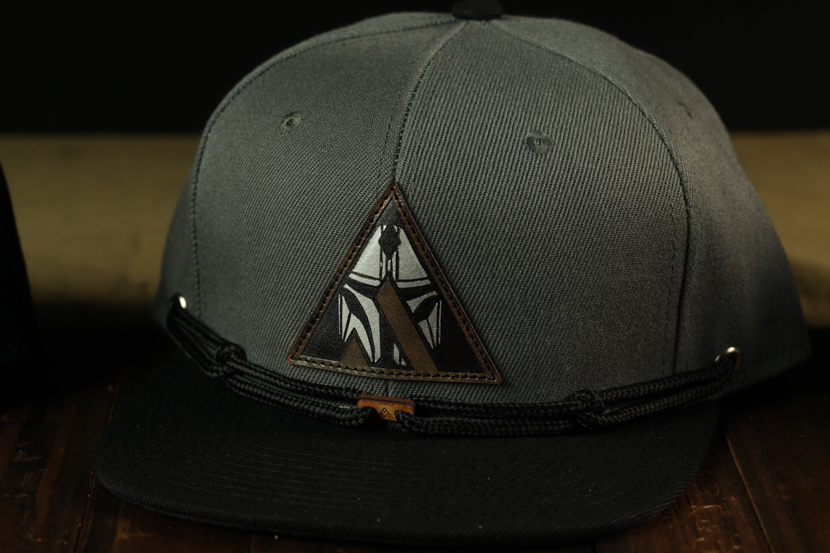 A black baseball cap with a triangular patch featuring a graphic design on the front.