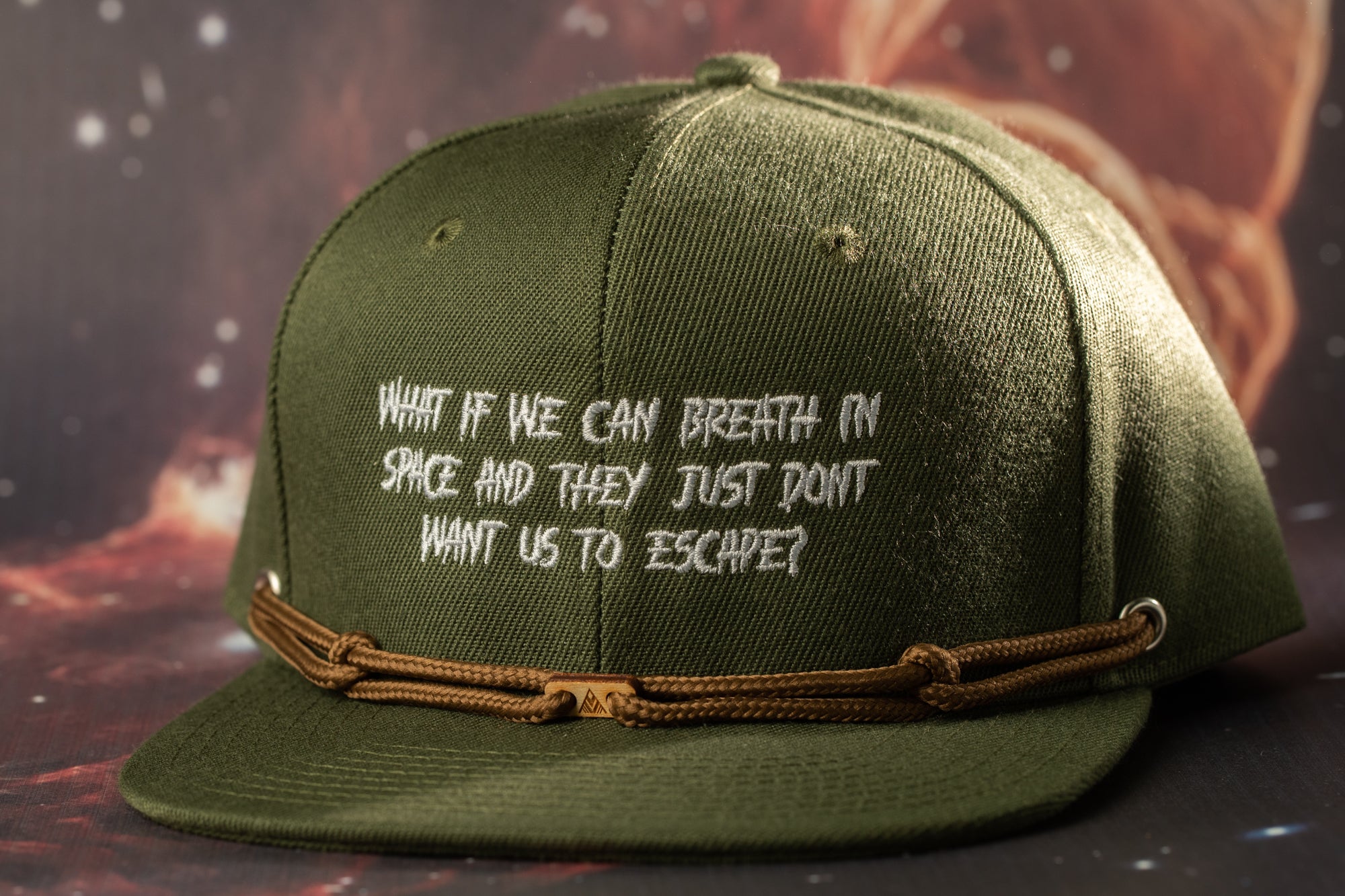 A green baseball cap with white text on it, which reads "What if we can breathe in space and they just don't want us to escape?"