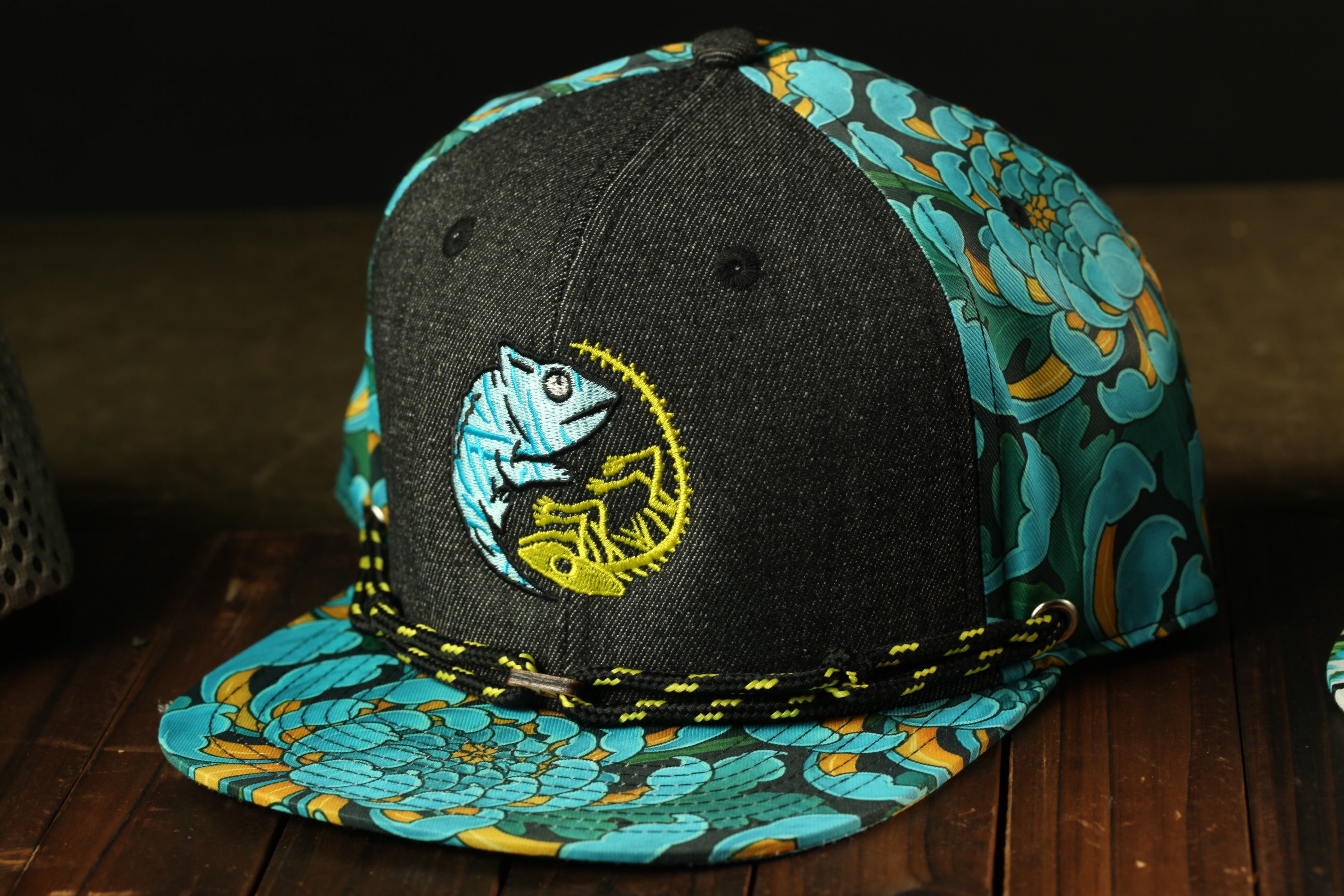 A black baseball cap with a colorful floral pattern and a chameleon design on the front.