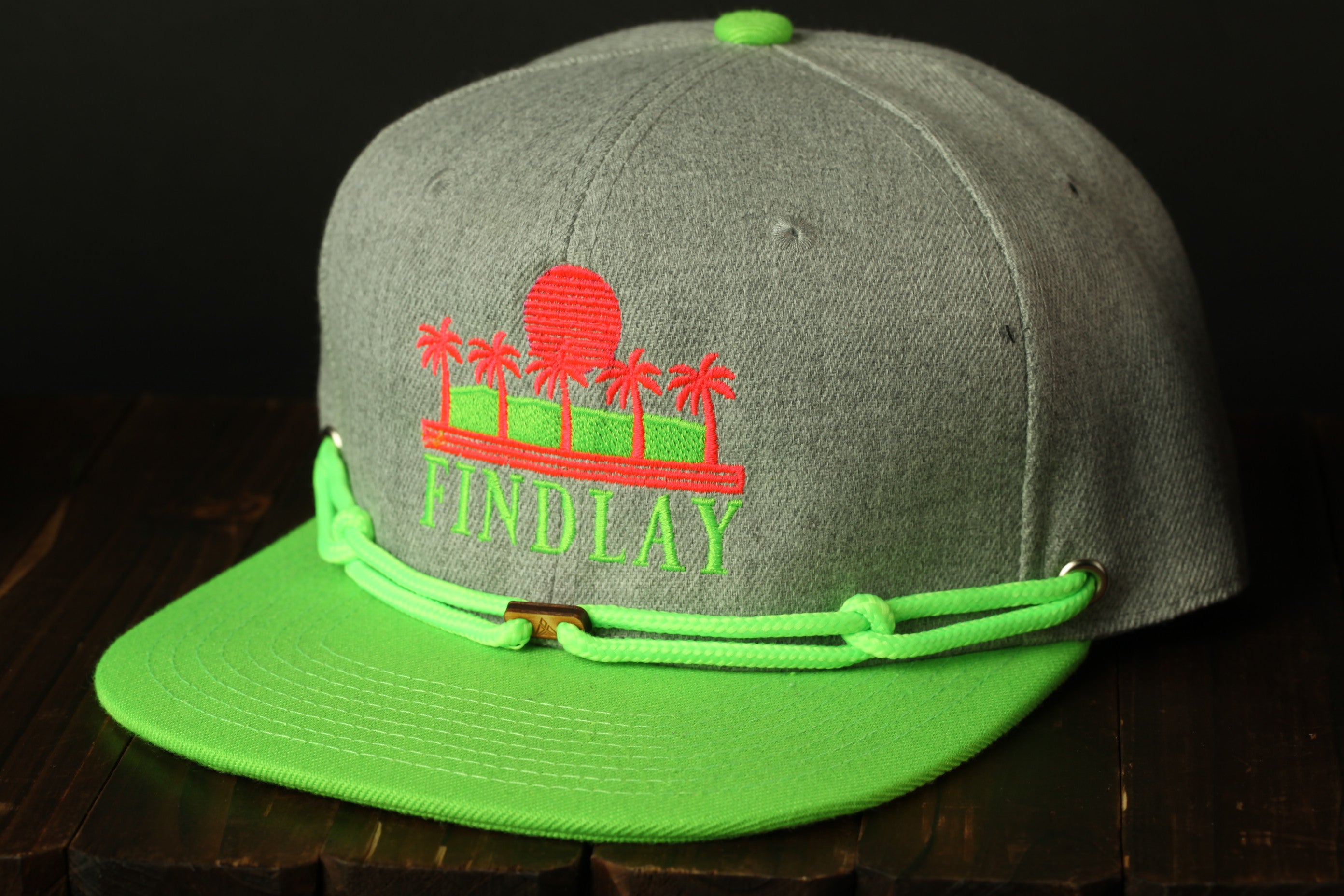 A grey baseball cap with a green brim and a graphic design on the front, sitting on a wooden surface.