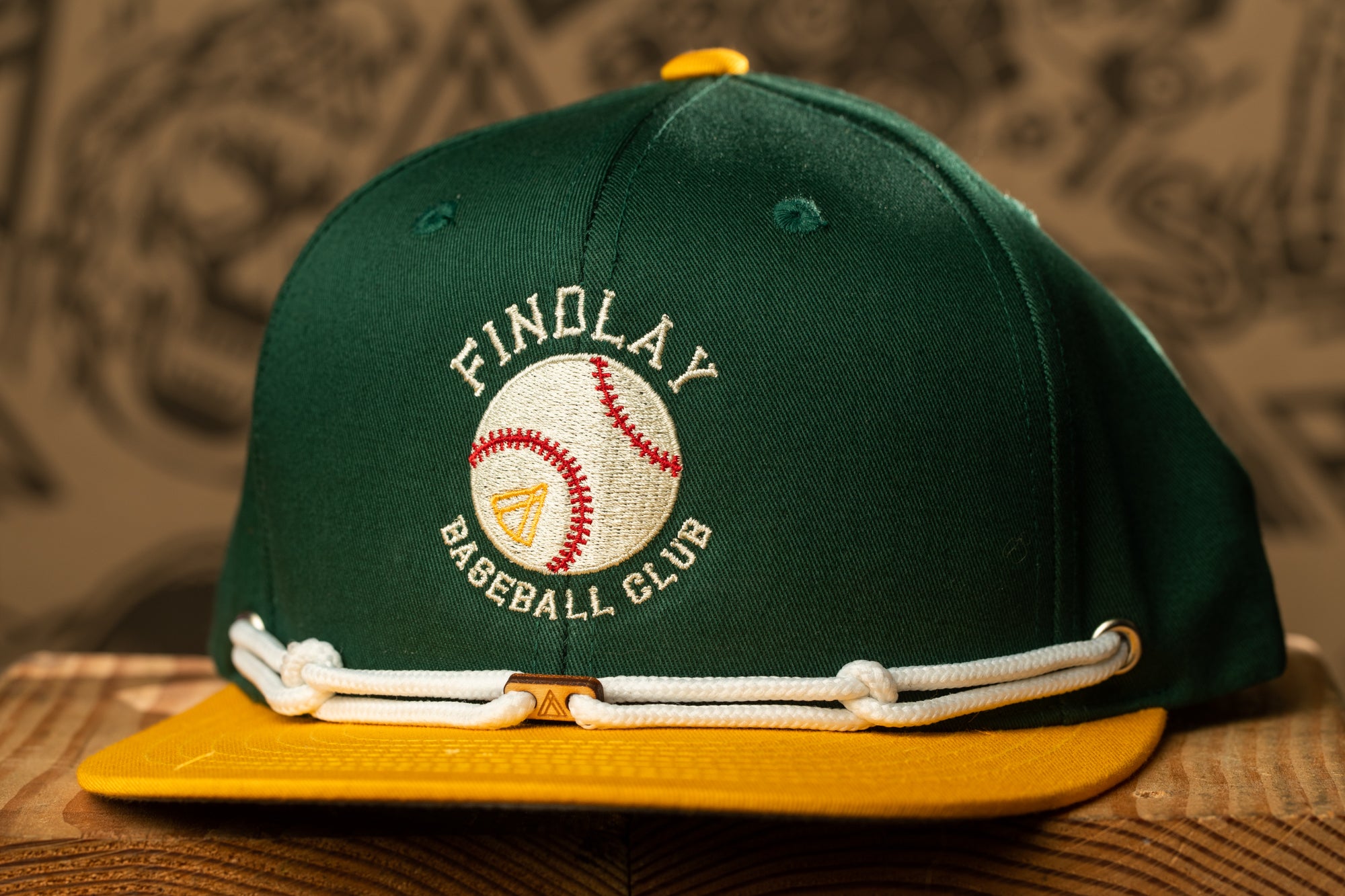 A green baseball cap with a white trim and a baseball logo on it, sitting on a wooden surface.