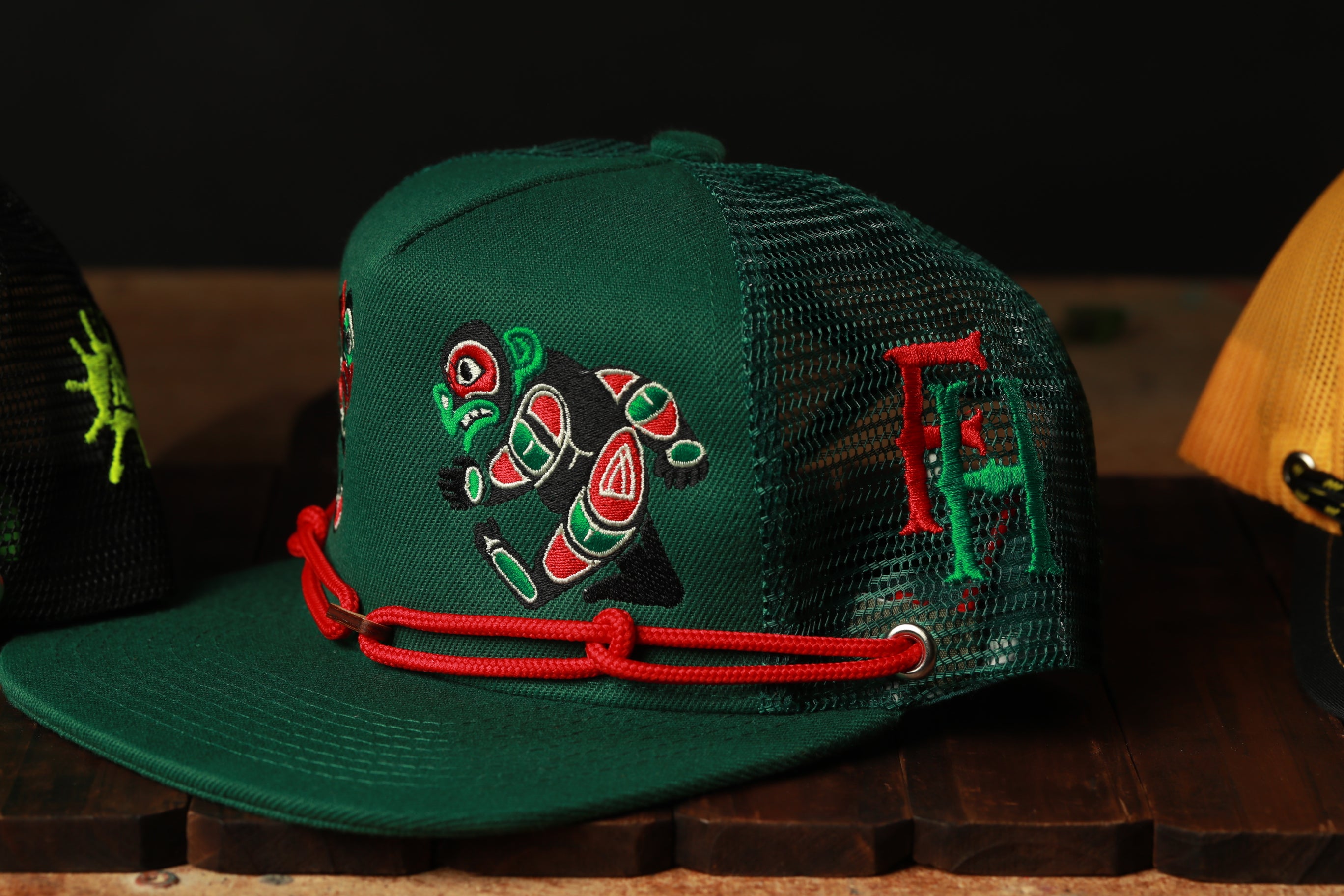 A green baseball cap with a red string and a colorful design on the front.
