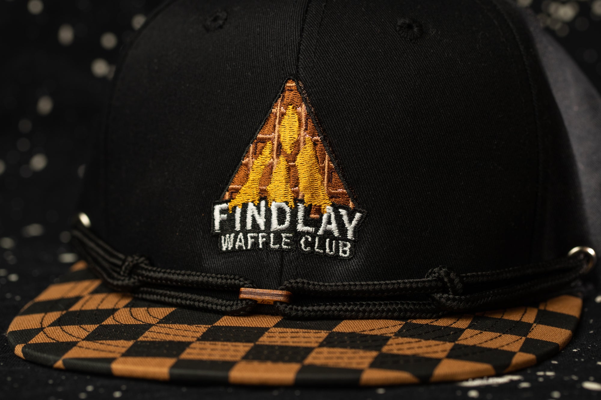 A black baseball cap with a checkered pattern and a logo on the front.