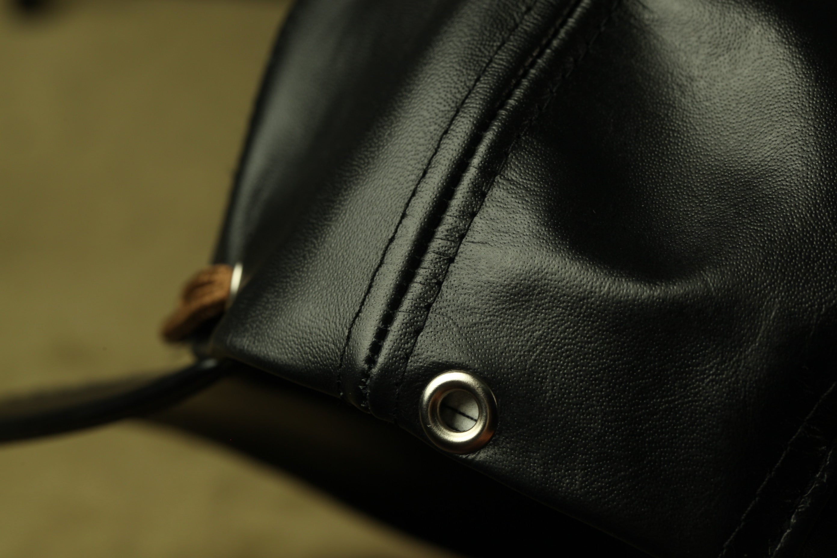 A close-up view of a black leather item, possibly a bag or wallet, with a metal button and a leather strap visible.