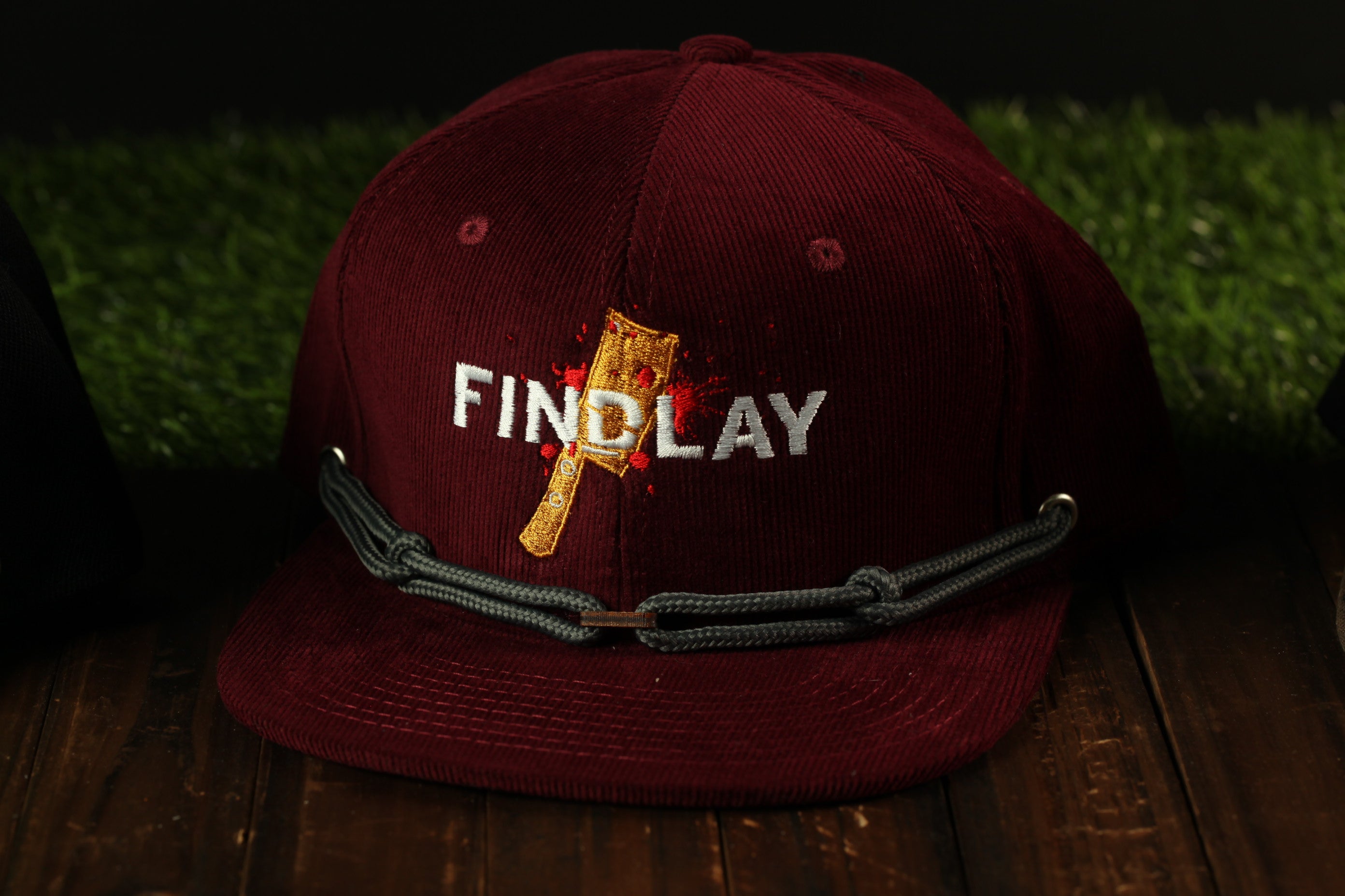 A burgundy baseball cap with the word "FINDLAY" printed on it, sitting on a wooden surface.