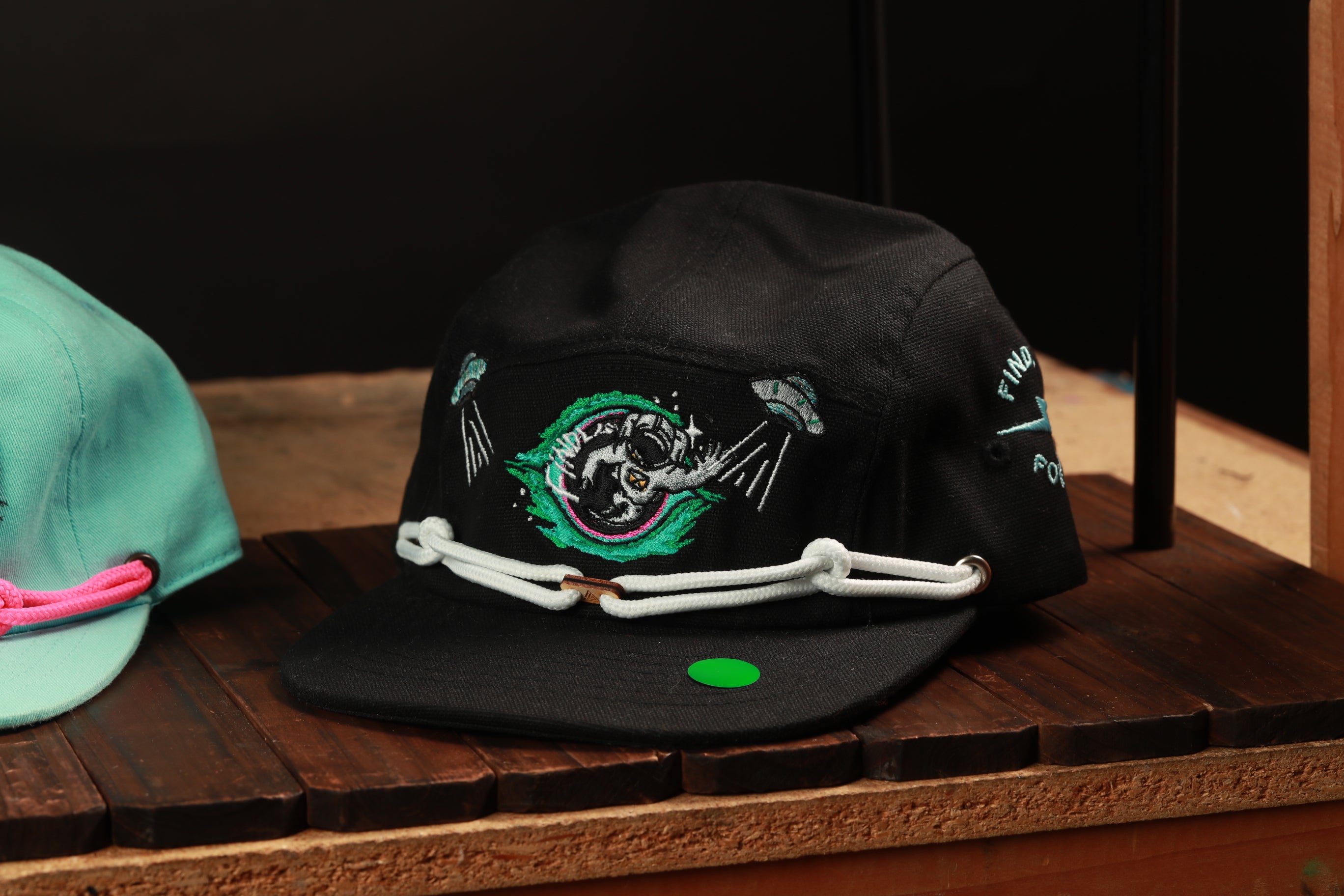 A black baseball cap with a green and white design on the front, sitting on a wooden surface.
