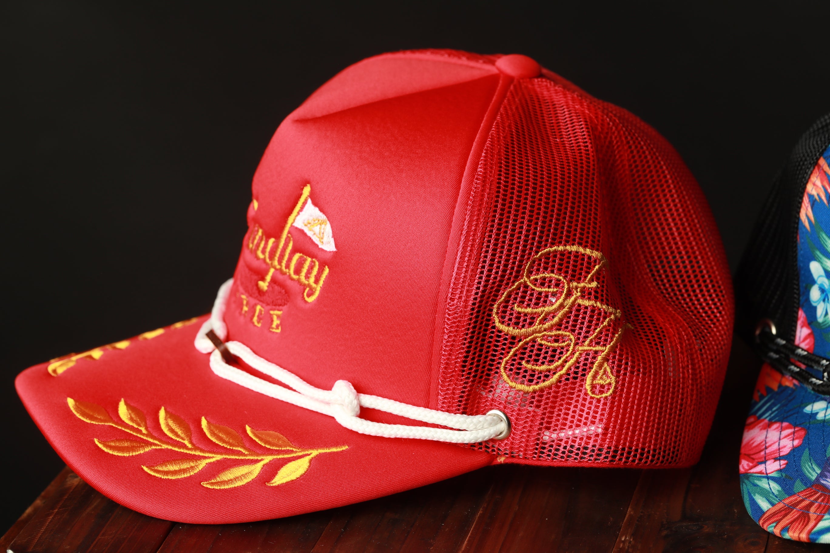 A red baseball cap with gold embroidered designs, including a leaf and a flag, is displayed on a wooden surface.