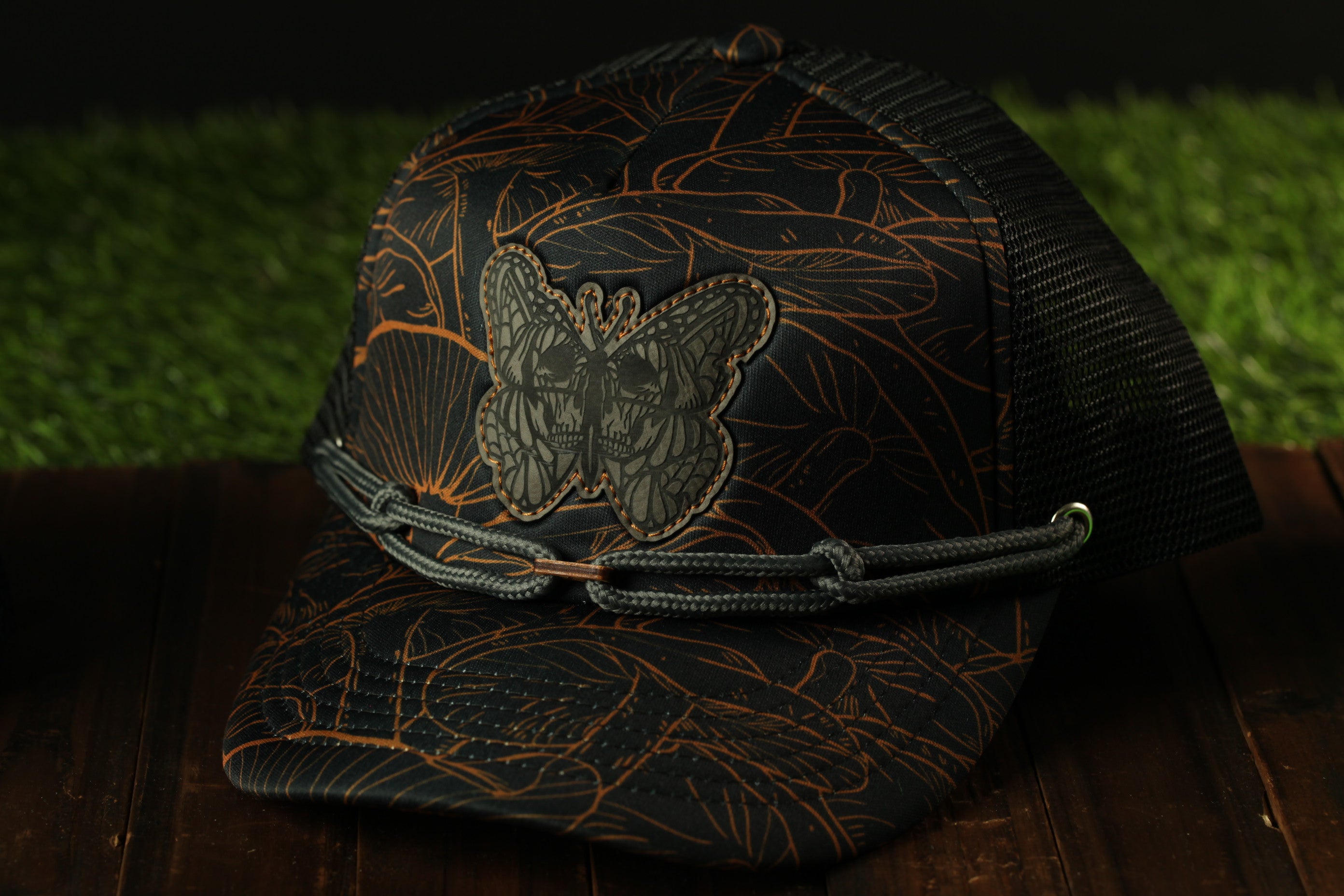 A black and orange patterned baseball cap with a butterfly design, resting on a wooden surface.