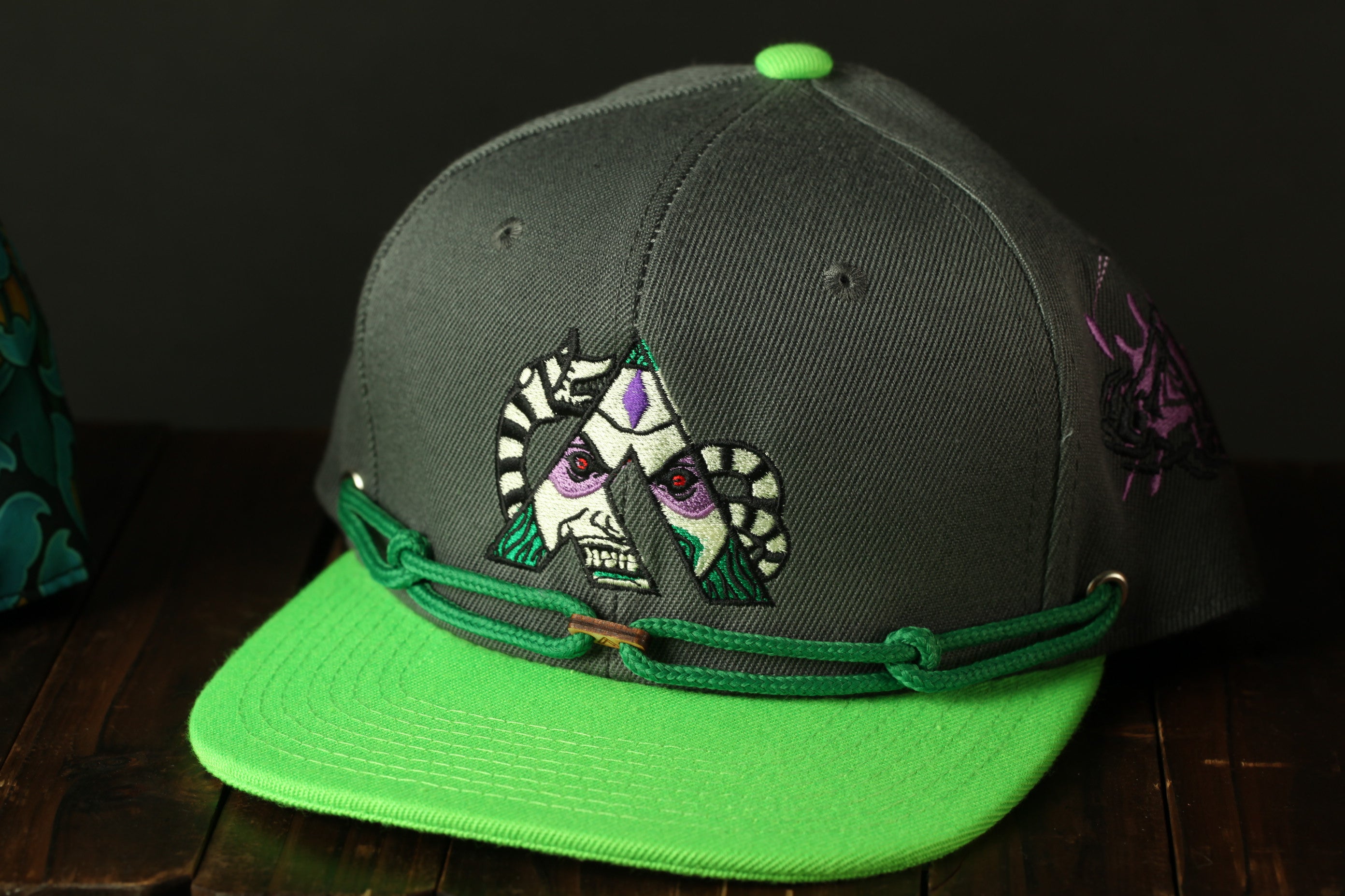 A dark green baseball cap with a green brim and a graphic design on the front, sitting on a wooden surface.
