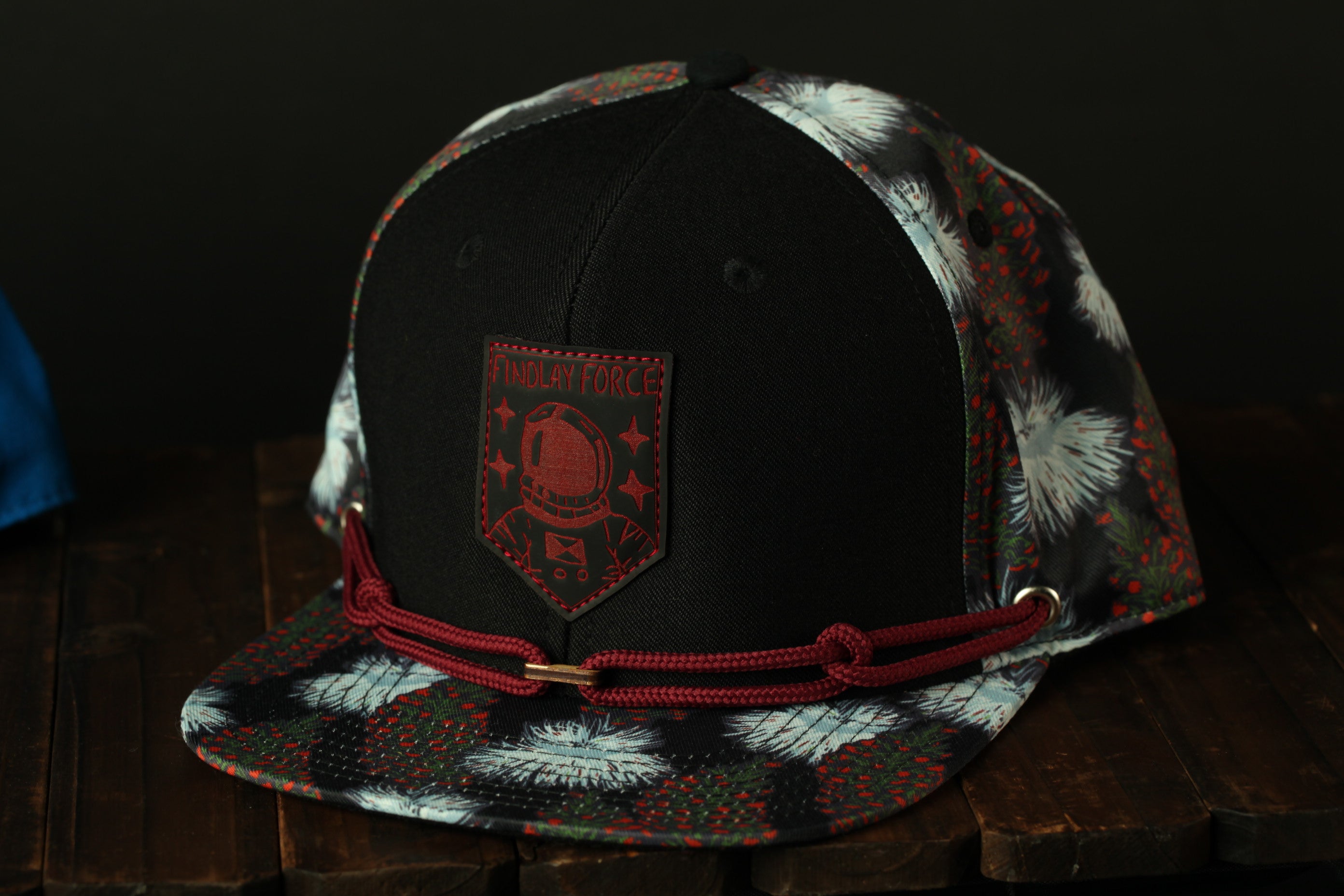 A black baseball cap with a red and white floral pattern, featuring a red patch with a red and white design and the text "TIMLAY FORCE" on the front.
